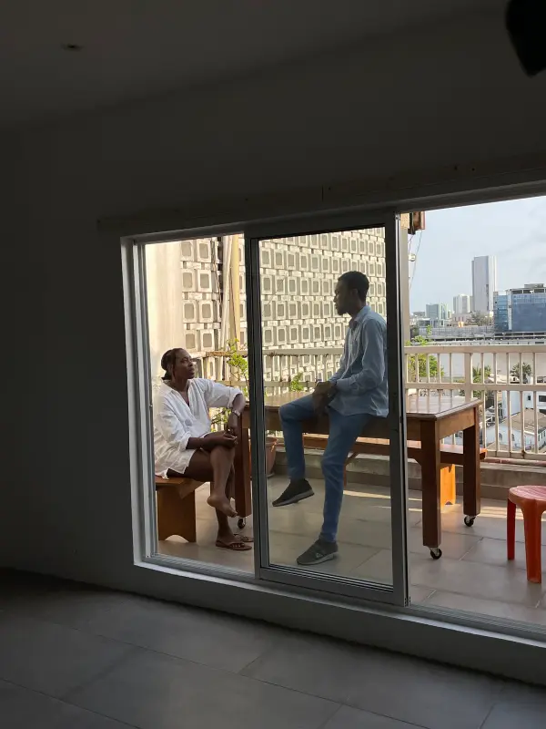 Two people having a relaxed conversation on a balcony overlooking an urban cityscape.