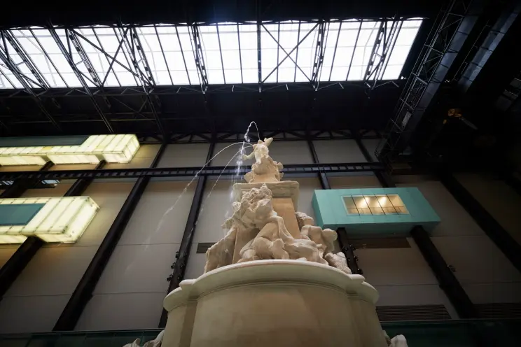 A towering white fountain captured from a frog perspective dominates a spacious gallery hall. The structure is carved intr...