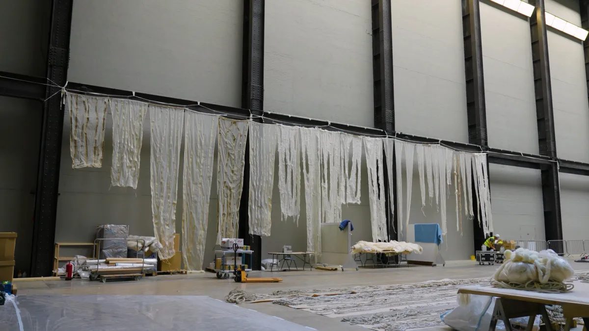 Strips of white tattered fabric hangs during an art installation.