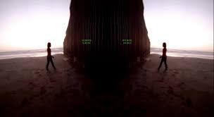 Two individuals standing outdoors with a distance between them, located on either side of a rugged, natural rock formation...
