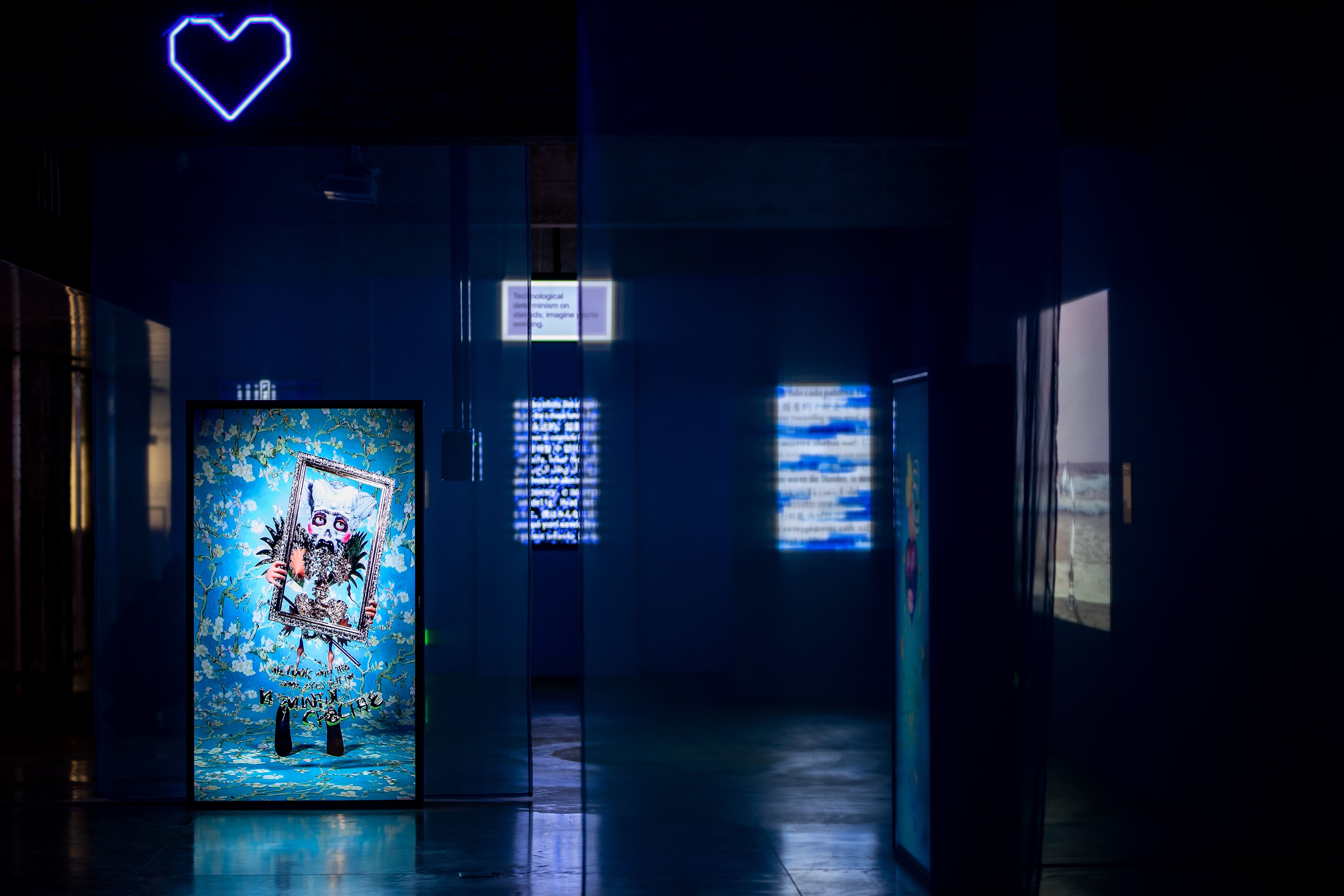Dark gallery with neon heart and monitors showcasing digital art.