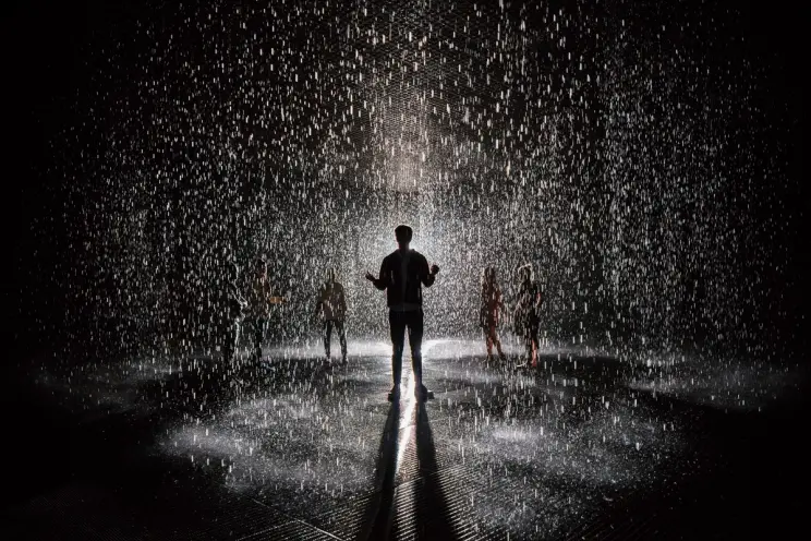 A silhouette of a person in the spotlight amidst heavy rain against a dark background, surrounded by multiple other vague ...