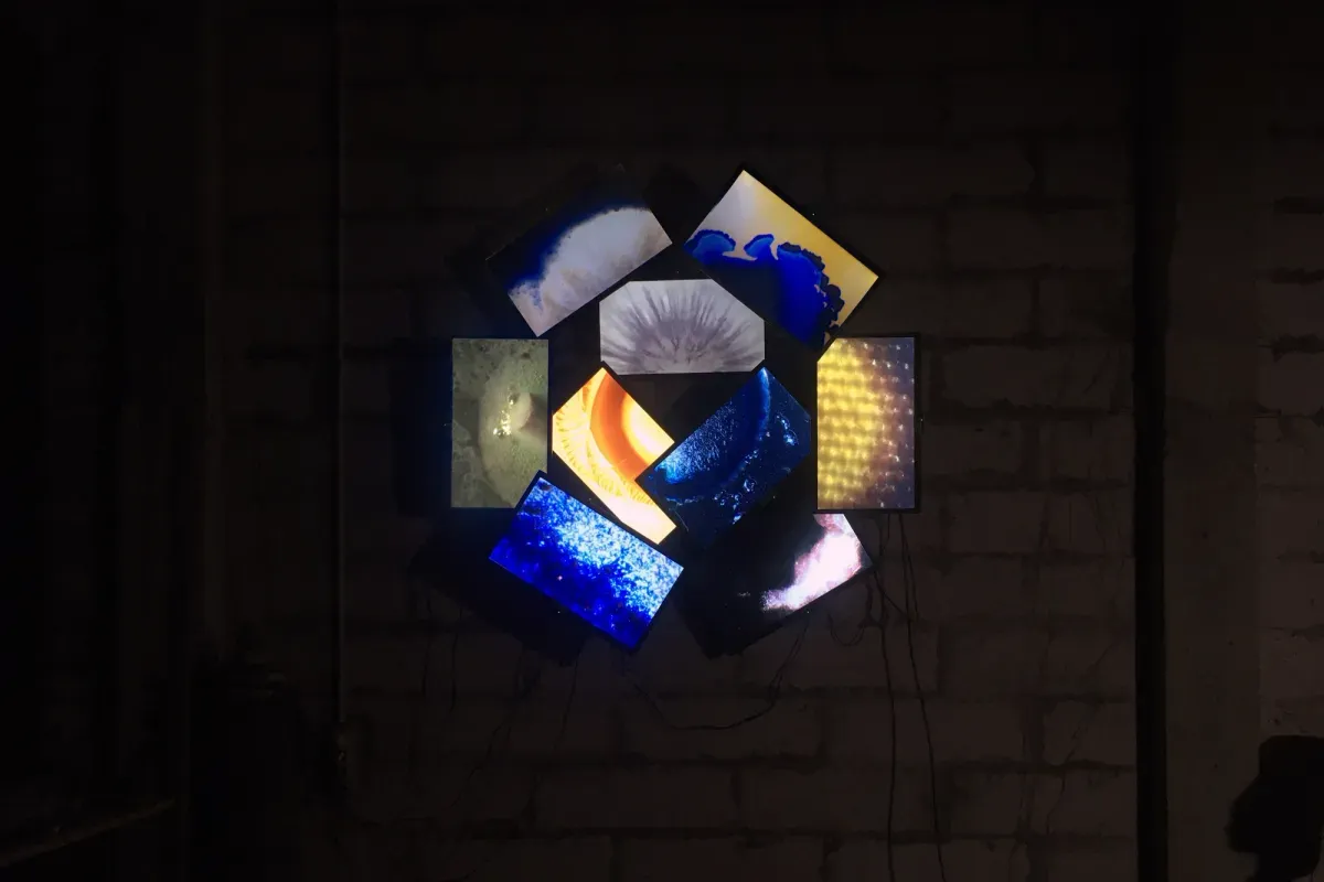 A 9-channel video installation resembling a flower, with monitors on the wall displaying abstract images.