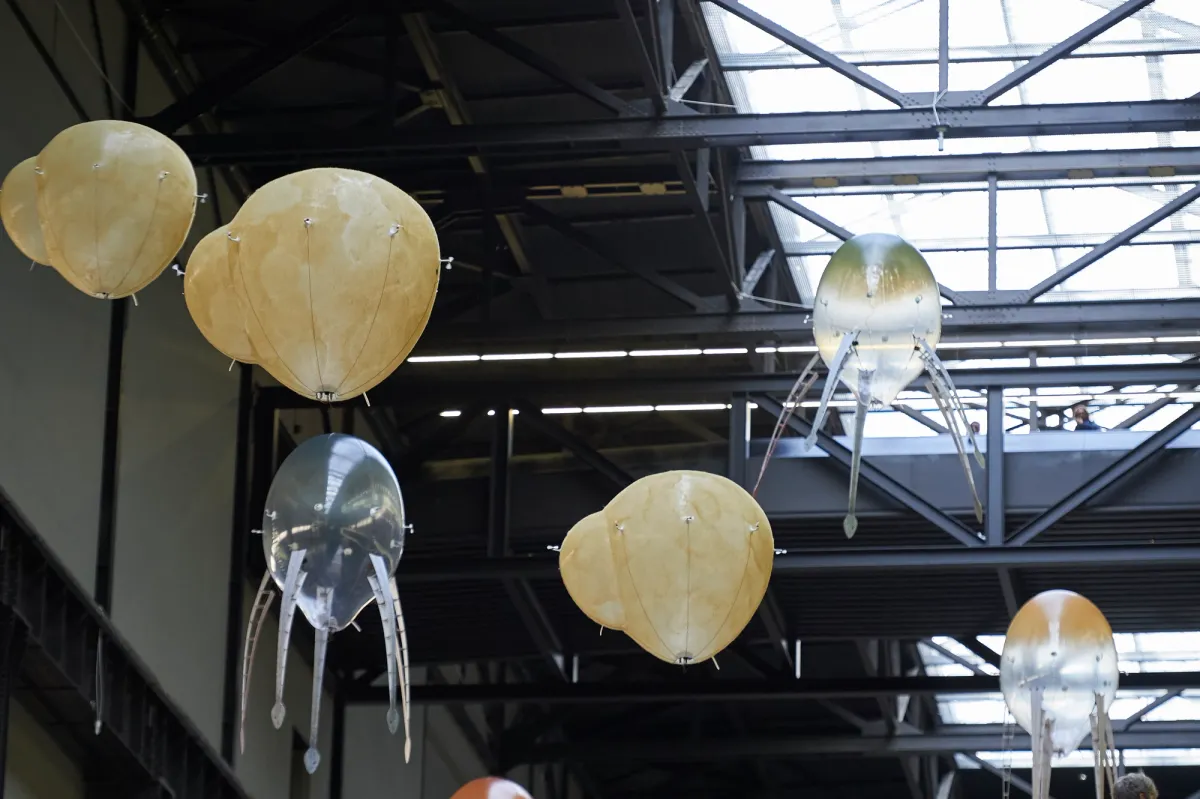 An industrial style installation featuring ceiling lamps shaped like an octopus with snake-headed tentacles. Additional yellowish round forms dangle from the ceiling.