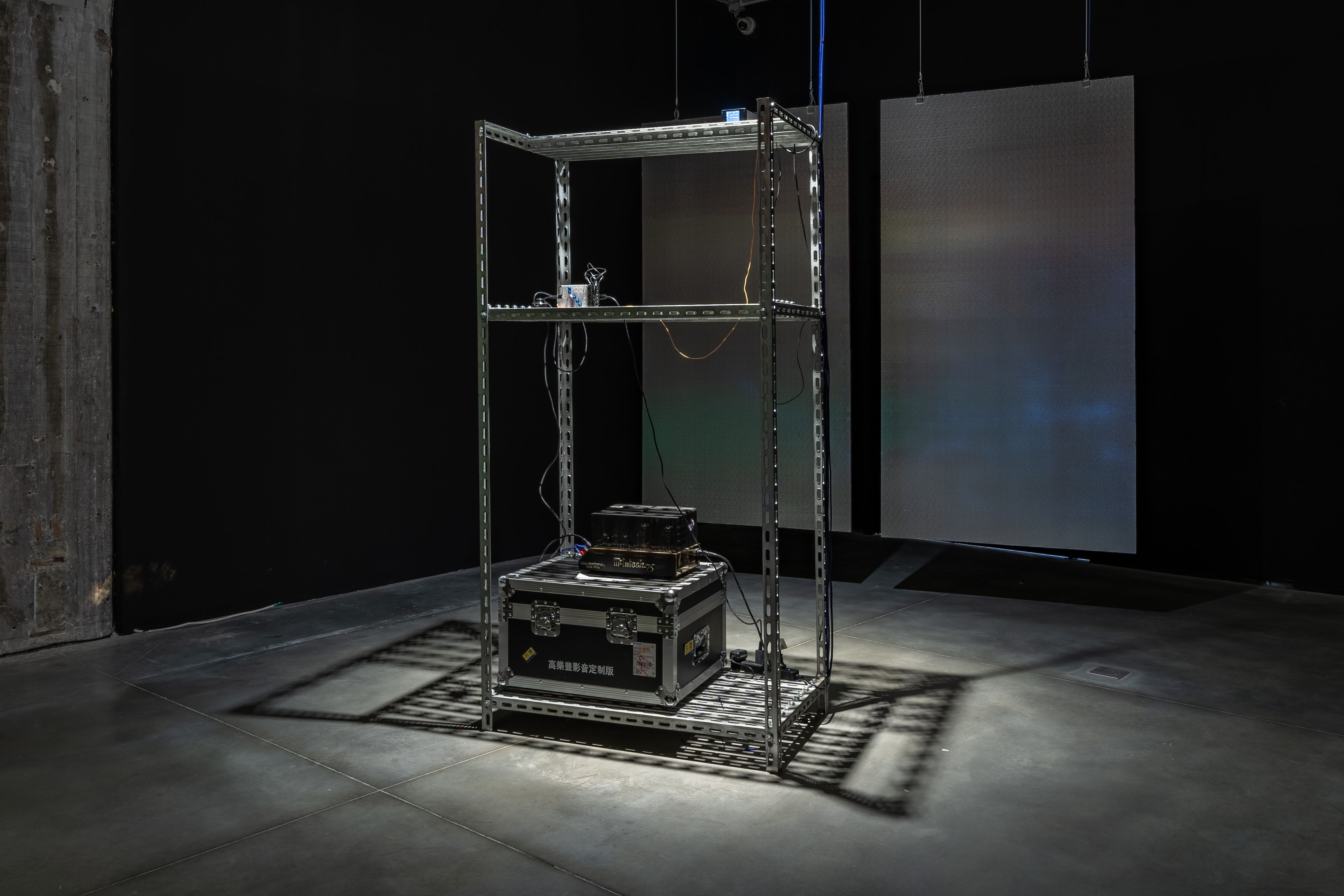 Art installation with metal frame and suspended panels in a dim room.