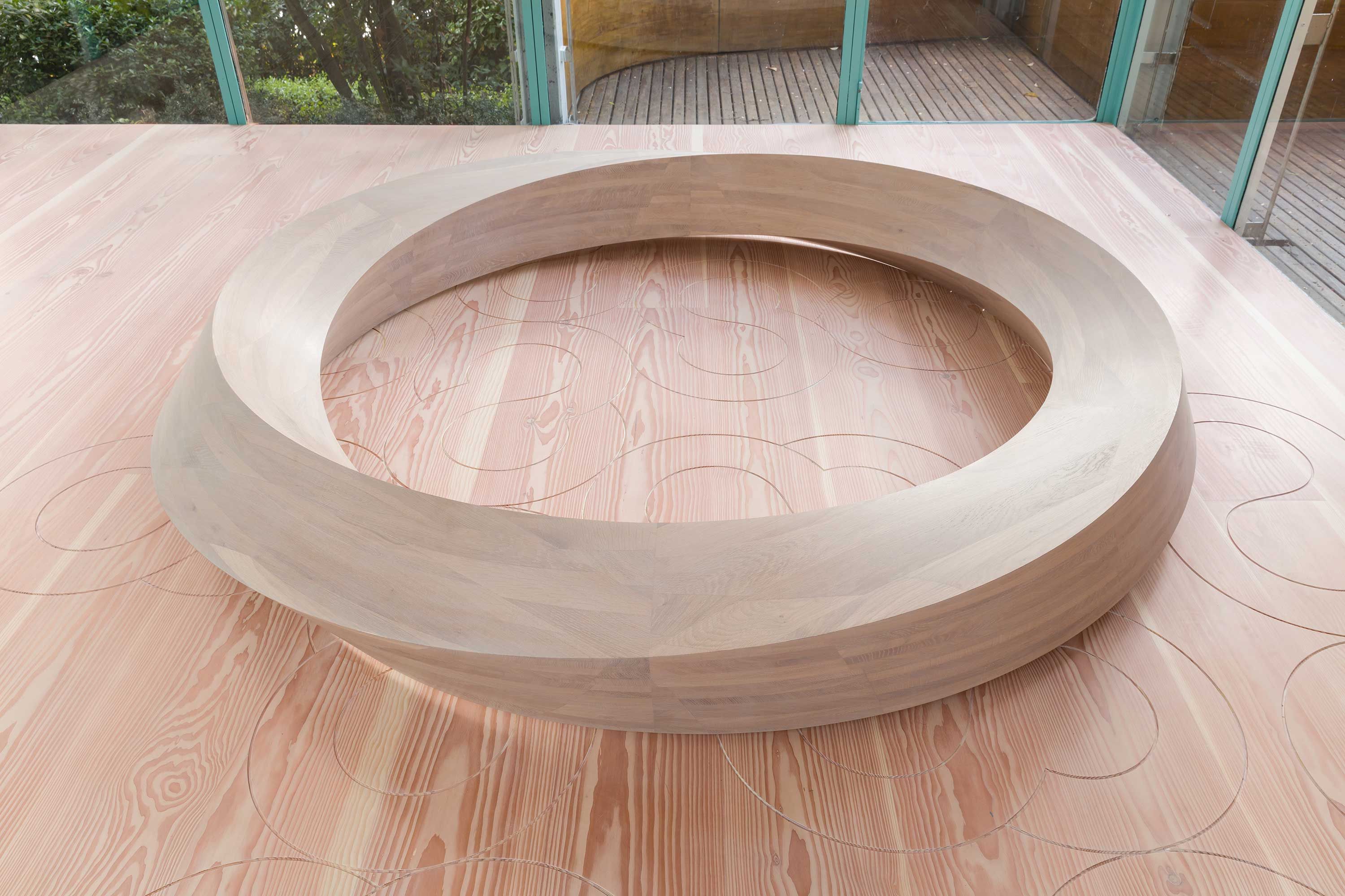 Close-up of a wooden ring sculpture on a wooden floor, highlighting its smooth finish and the intricate wood grain.