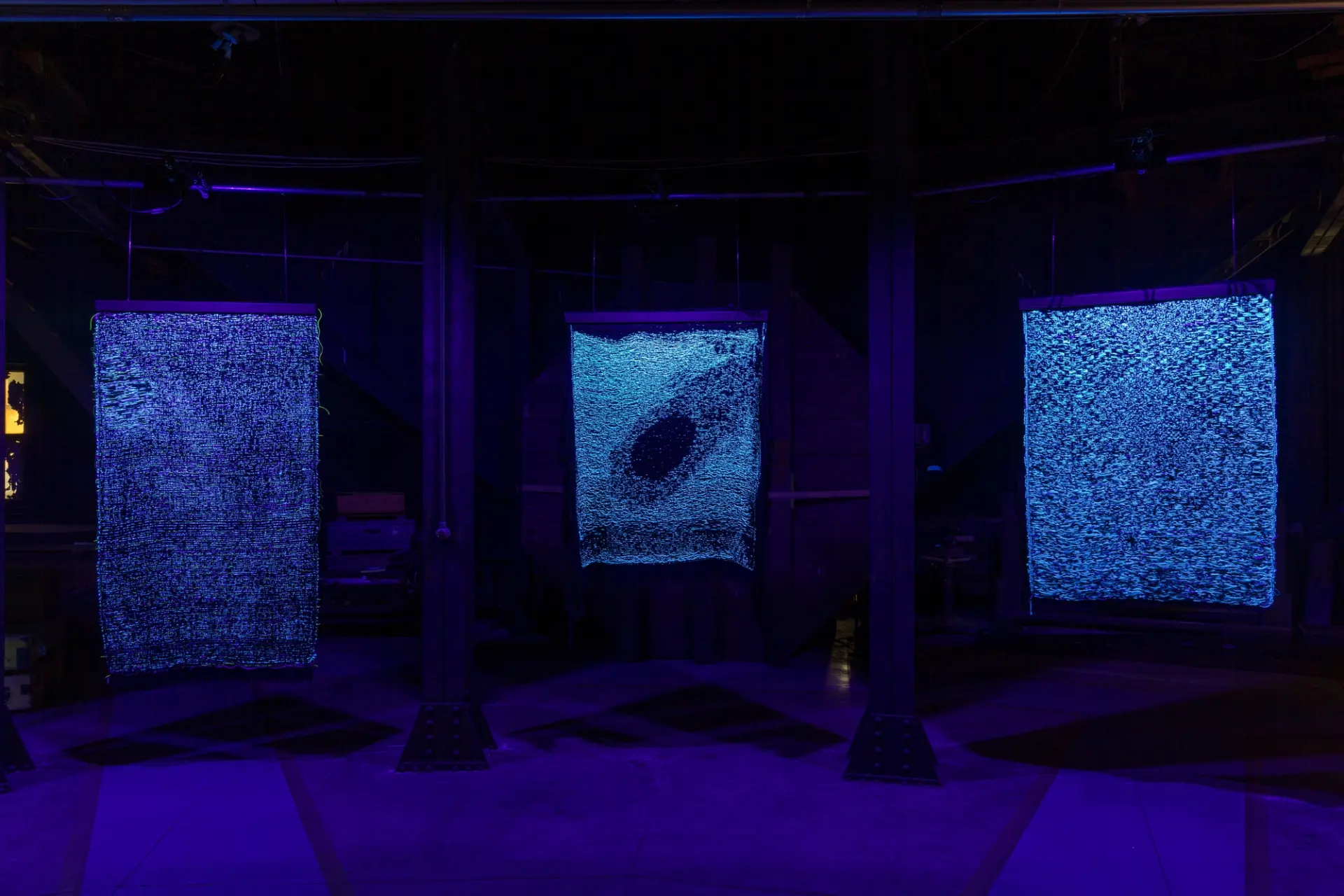 Three tapestry artworks displayed in a room bathed in soft blue light.