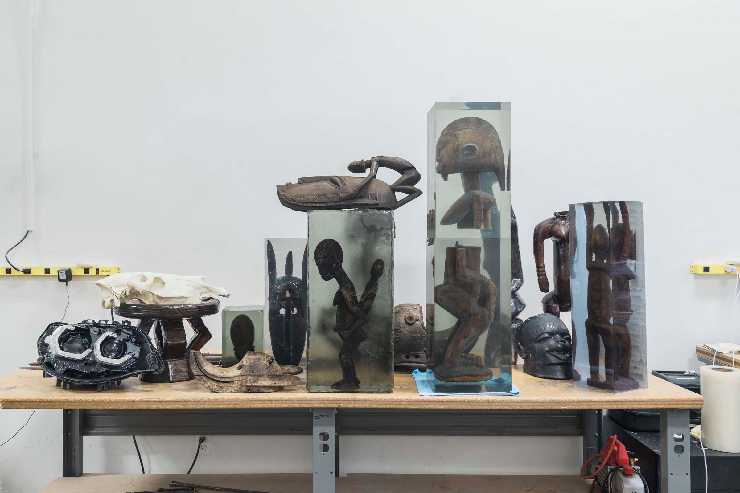 A workshop table populated with a variety of unique sculptures in an array of shapes and materials, set in an artist's stu...