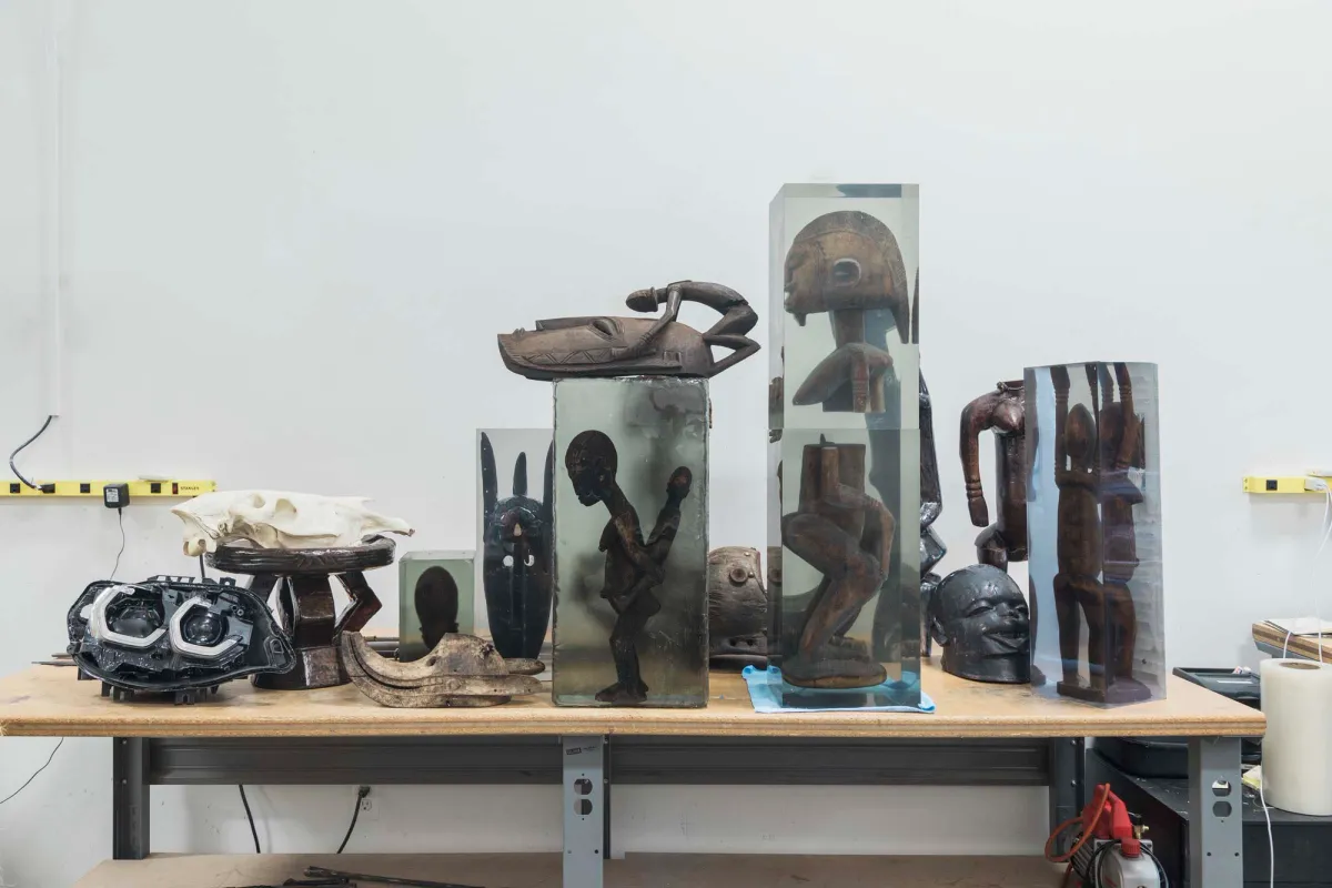 A workshop table populated with a variety of unique sculptures in an array of shapes and materials, set in an artist's studio.