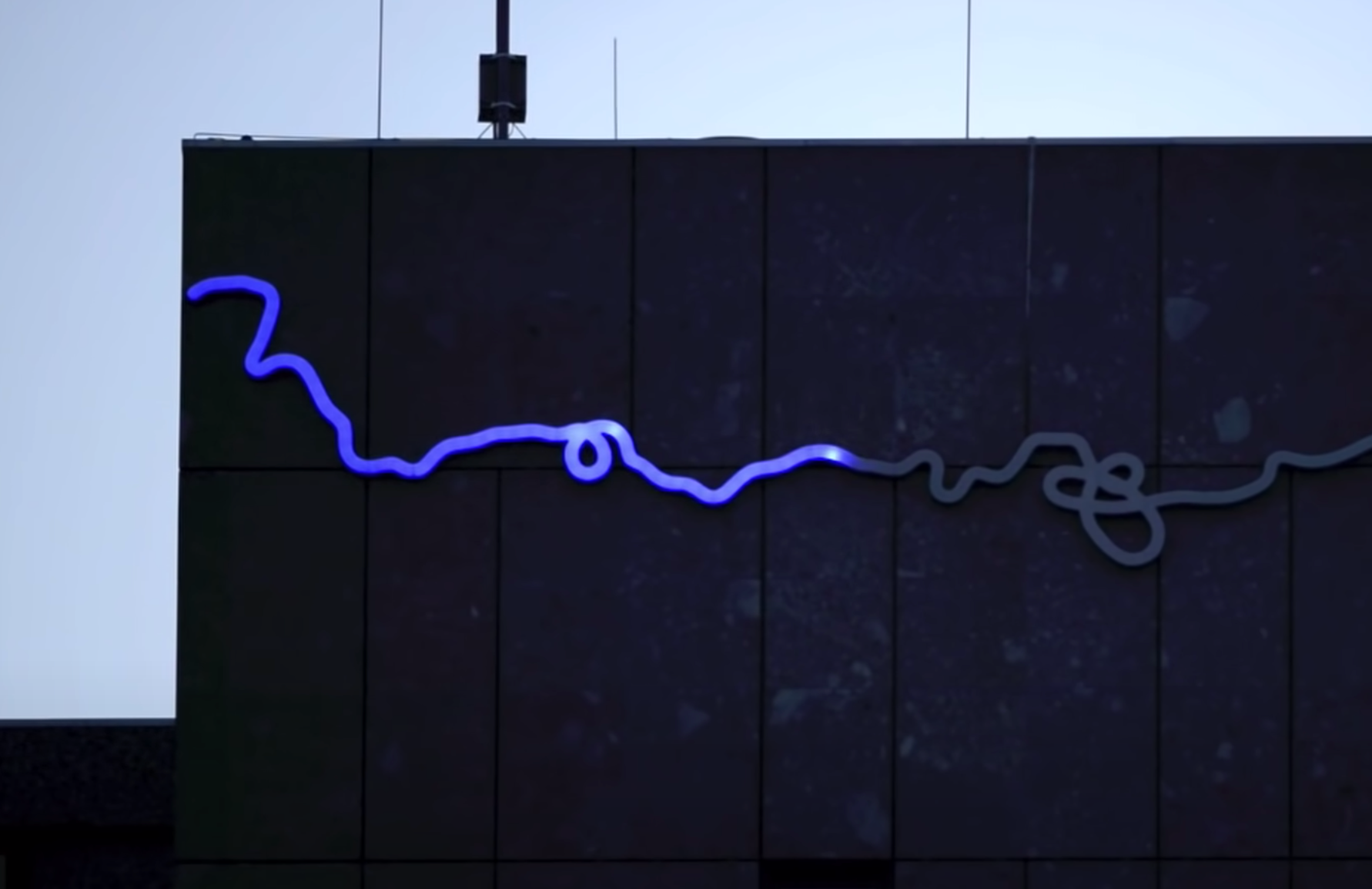 A black billboard featuring a horizontal line that bends subtly, transitioning from blue to grey, akin to a loading progre...