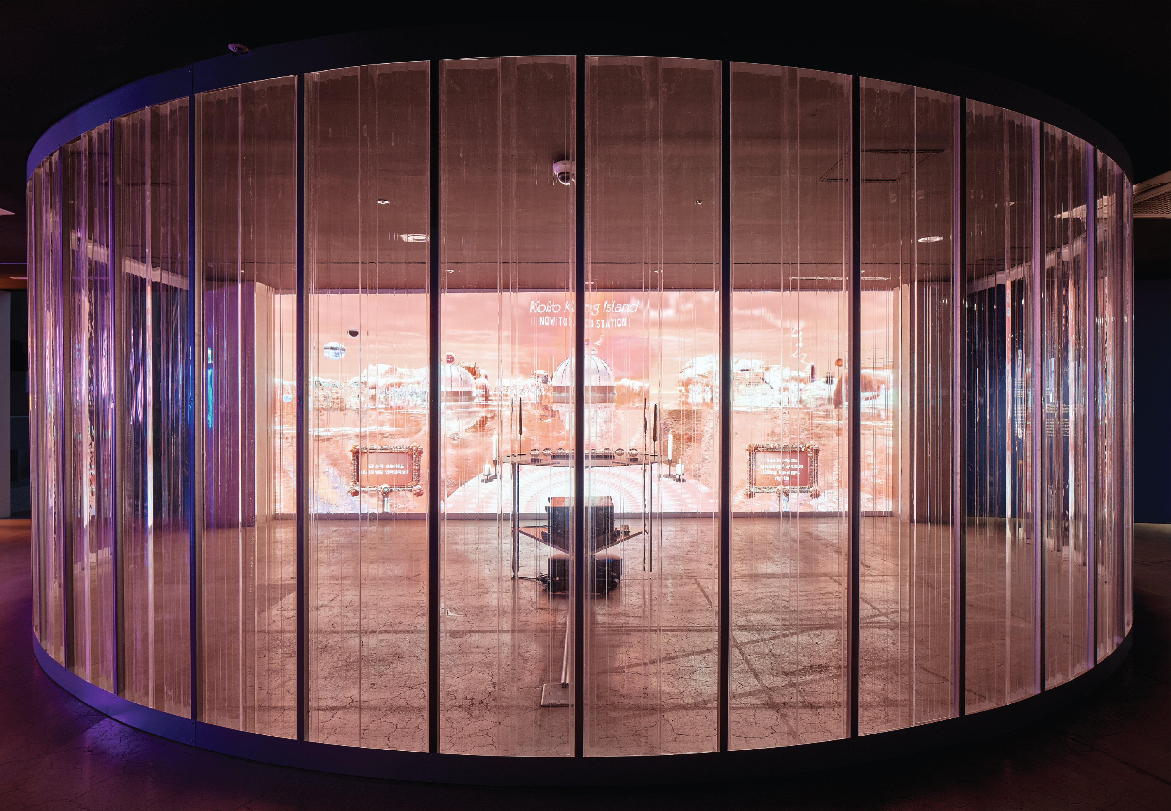 A round room with glass walls features a large screen positioned in front of a desk.