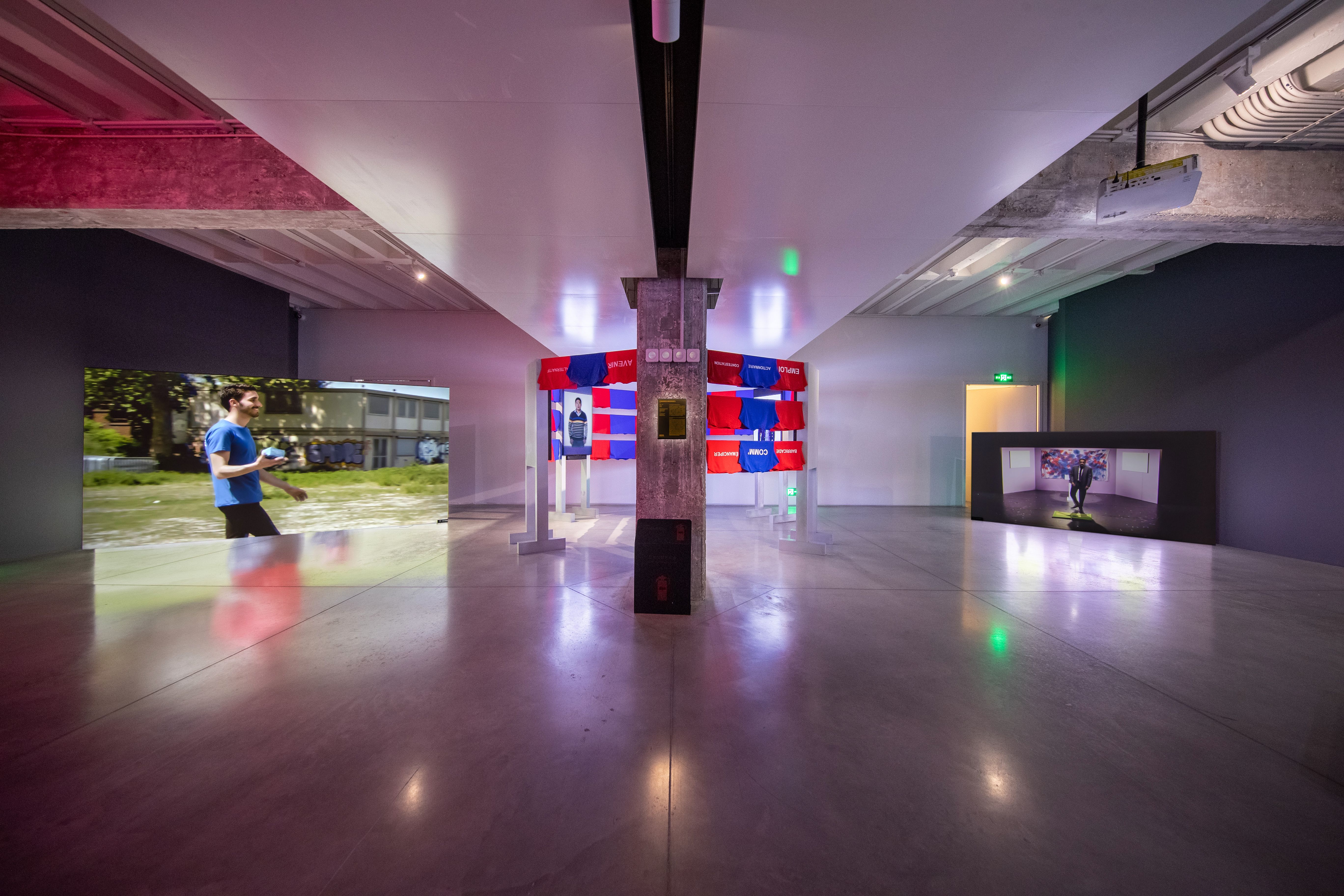 Spacious gallery with colorful fabric installation and video screens.