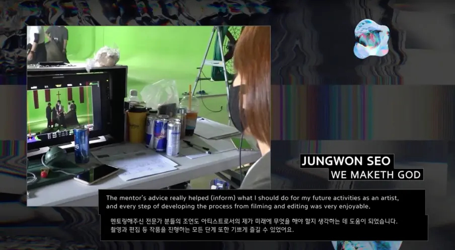 Artist Jungwon Seo sits at a desk in front of a video display, wearing a face mask. The display features a quote from Seo ...