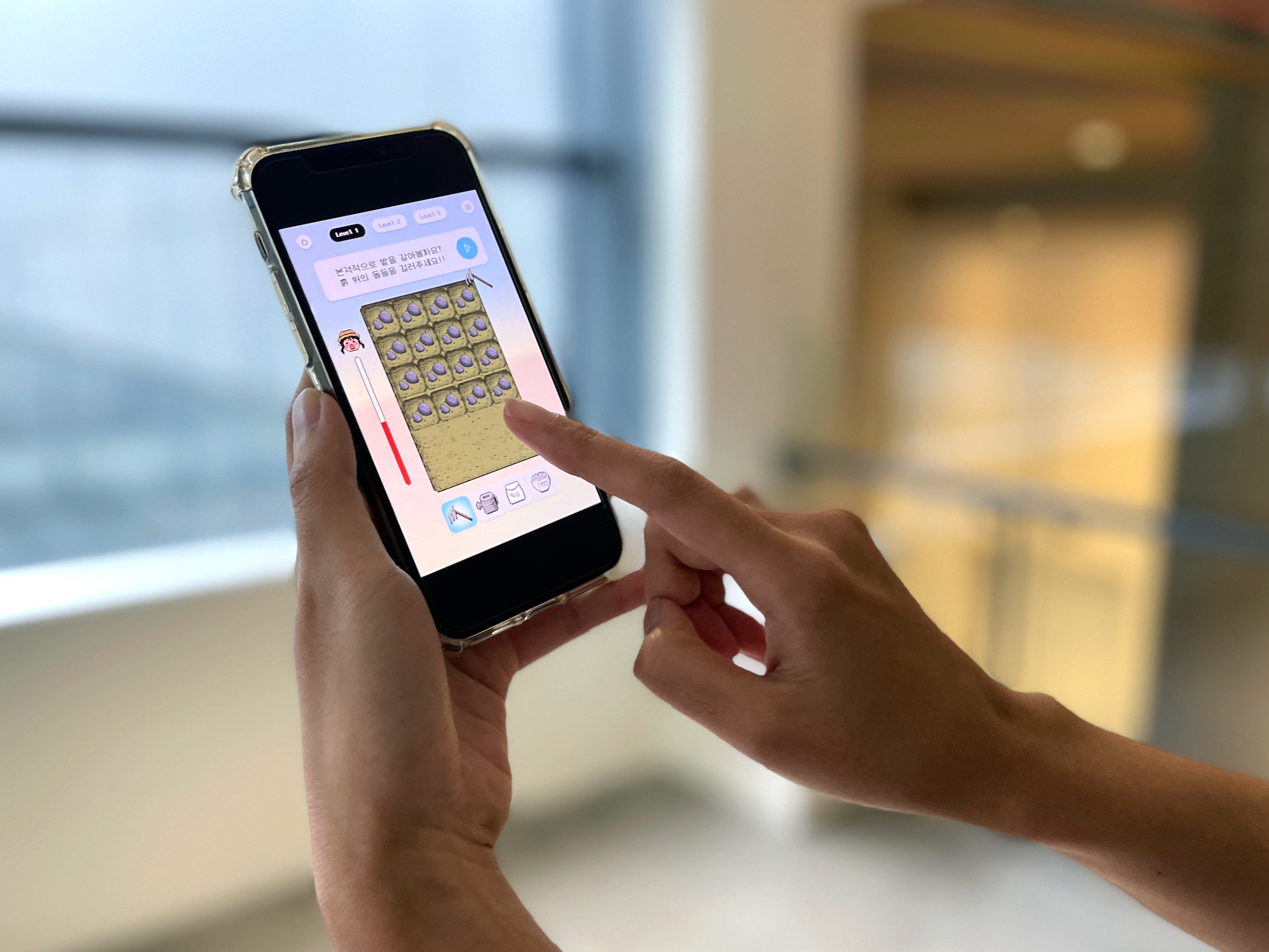Close-up of a person's hands using an iPhone with a game app open, in a light-filled room.