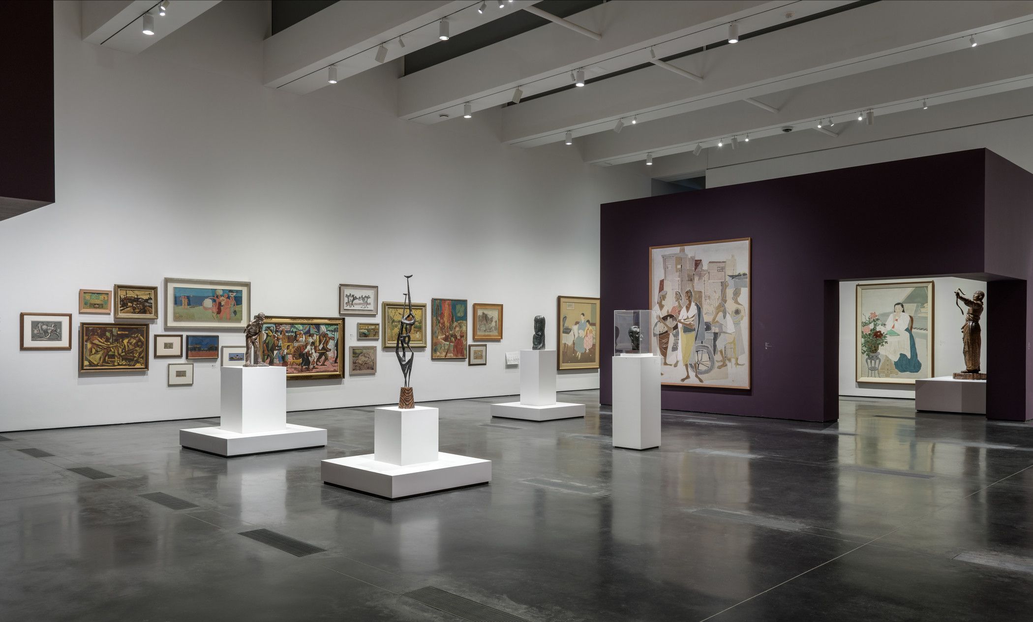 An art gallery room showcasing various art pieces on white cubicles centrally positioned, set against a distinct purple ex...