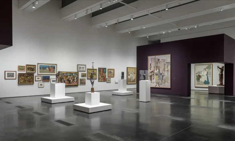 An art gallery room showcasing various art pieces on white cubicles centrally positioned, set against a distinct purple ex...