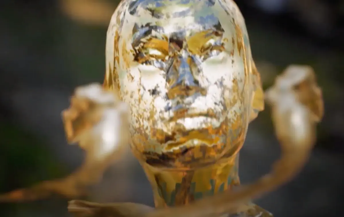 Close-up of a golden statue head, set against a softly blurred background.