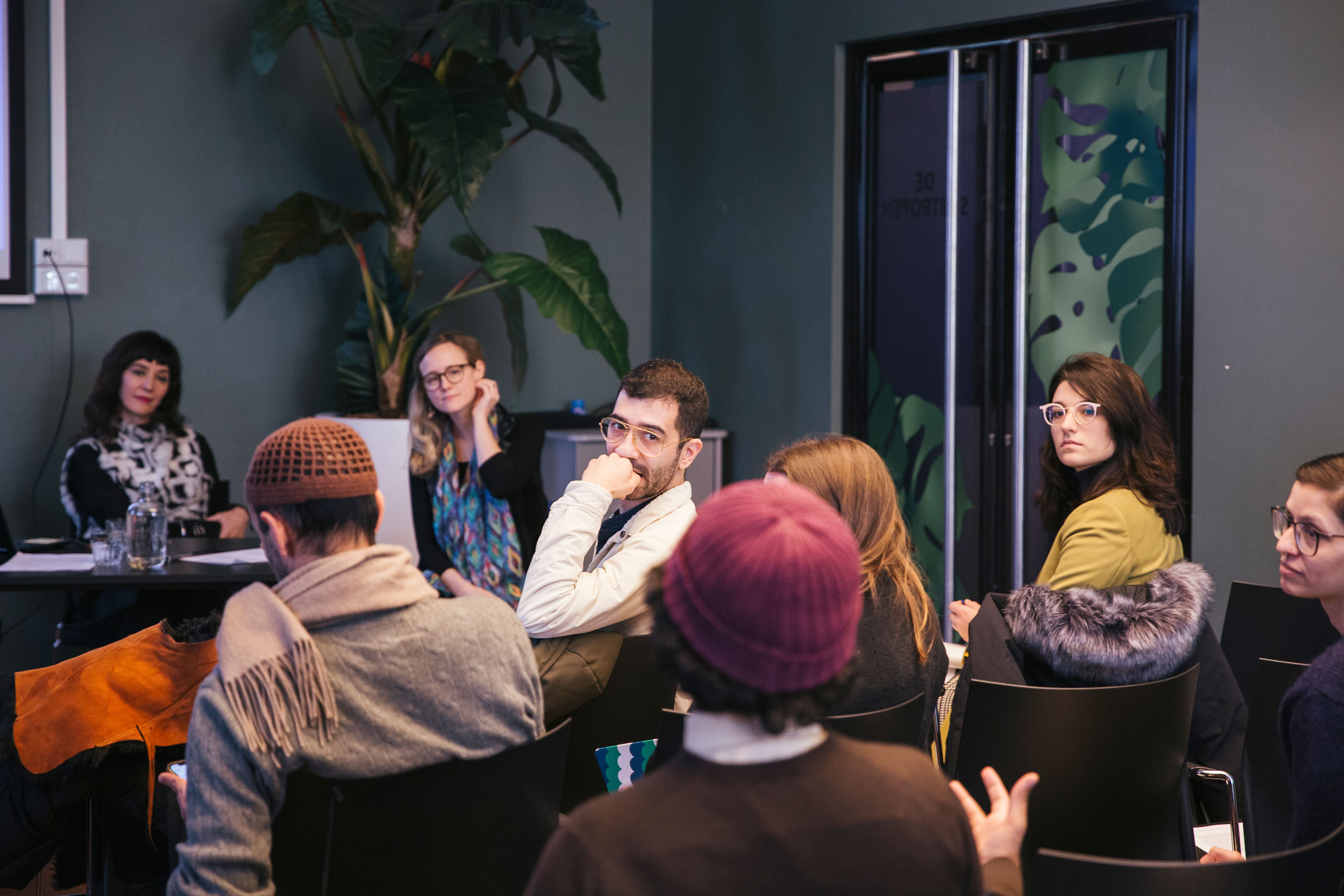 A seated audience in discussion in a room with dark green walls.
