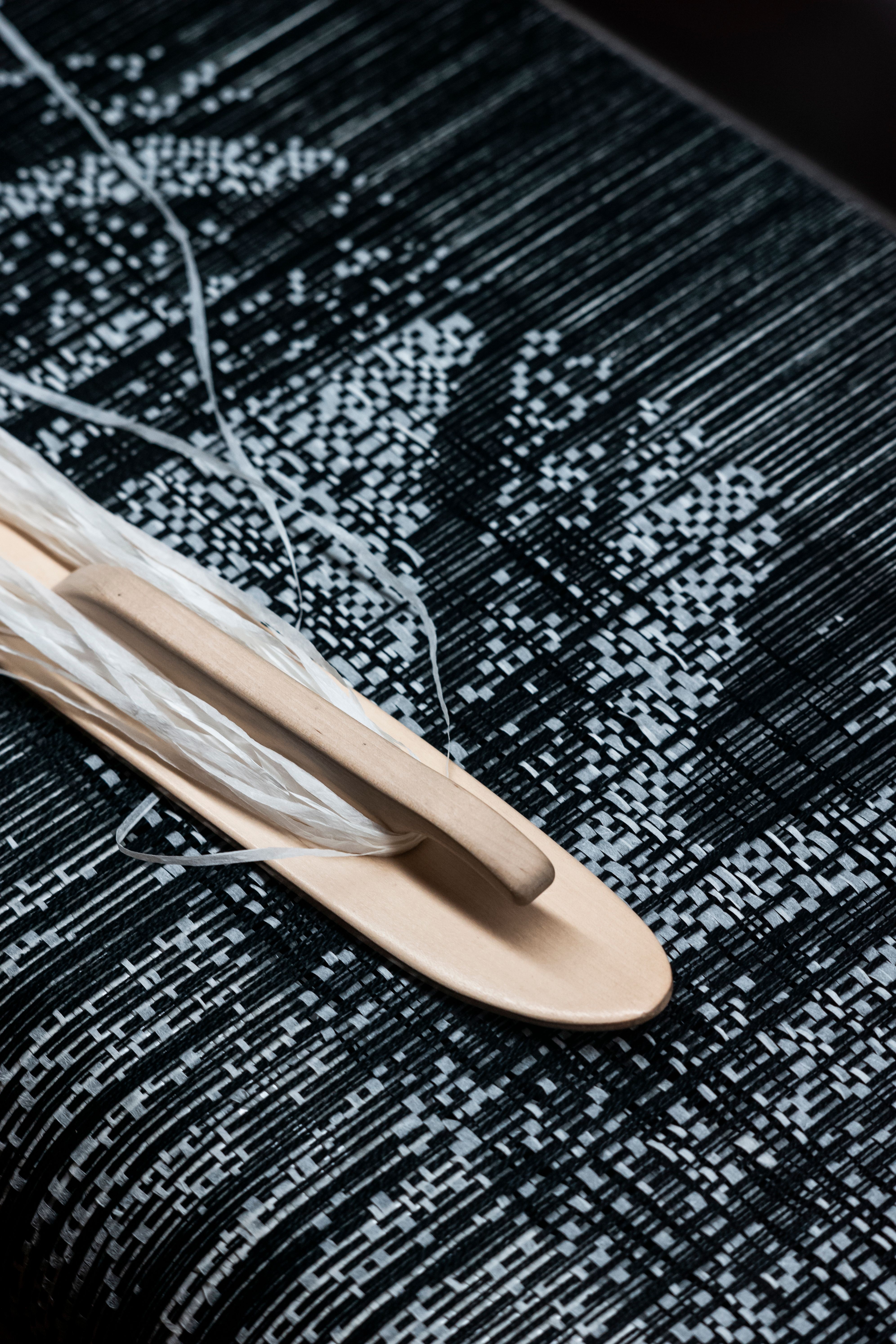 A shuttle with threads on black-and-white woven textile, showing detailed patterns.