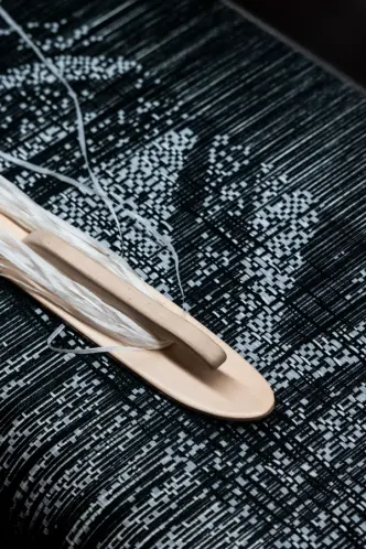 A shuttle with threads on black-and-white woven textile, showing detailed patterns.