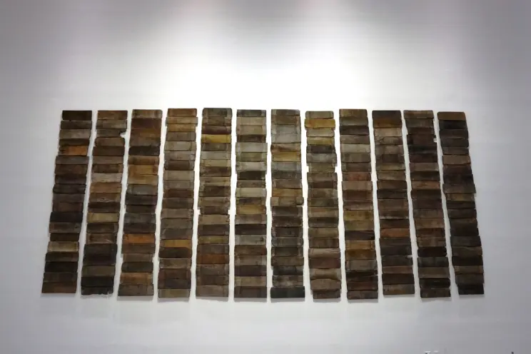 Several panels resembling wood are arranged in a grid on a pristine white wall, giving the appearance of a large-scale art...