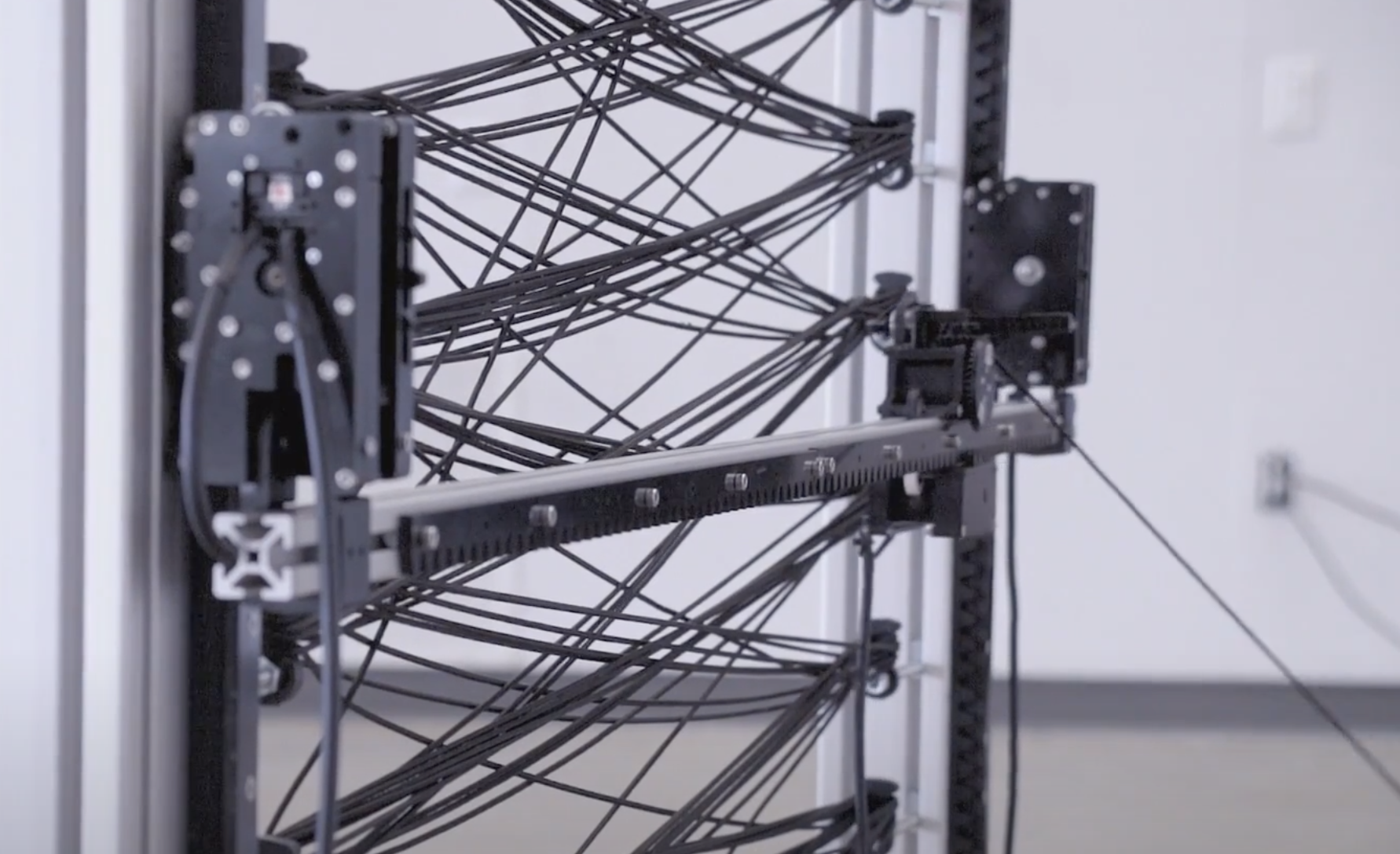 A metallic, spider-like robotic installation with black strings connecting its two ends, creating an intricate web-like de...