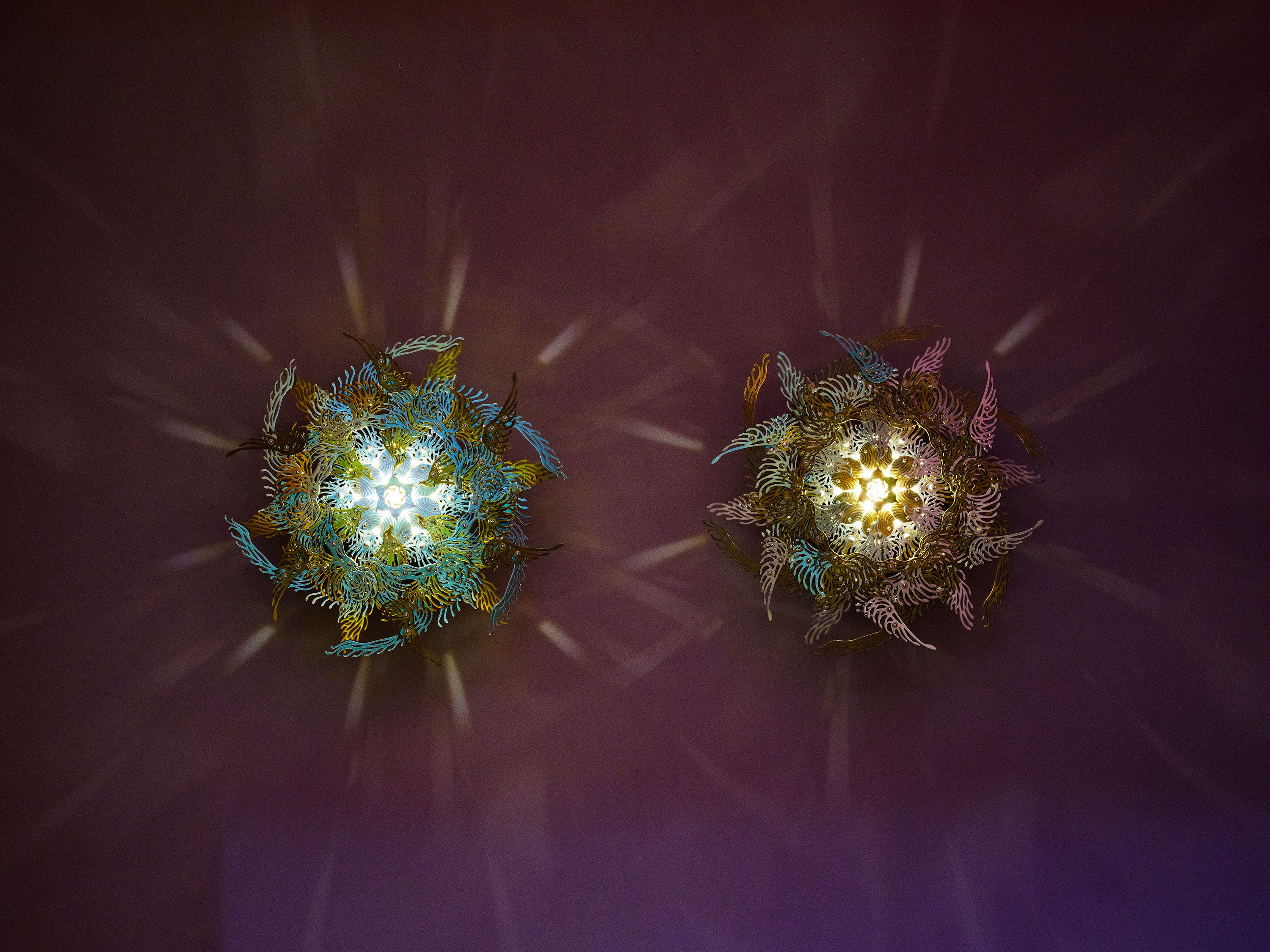 Two metallic, plant-like sculptures glowing in the dark, intricately designed with machinery and LED lights, creating a ca...