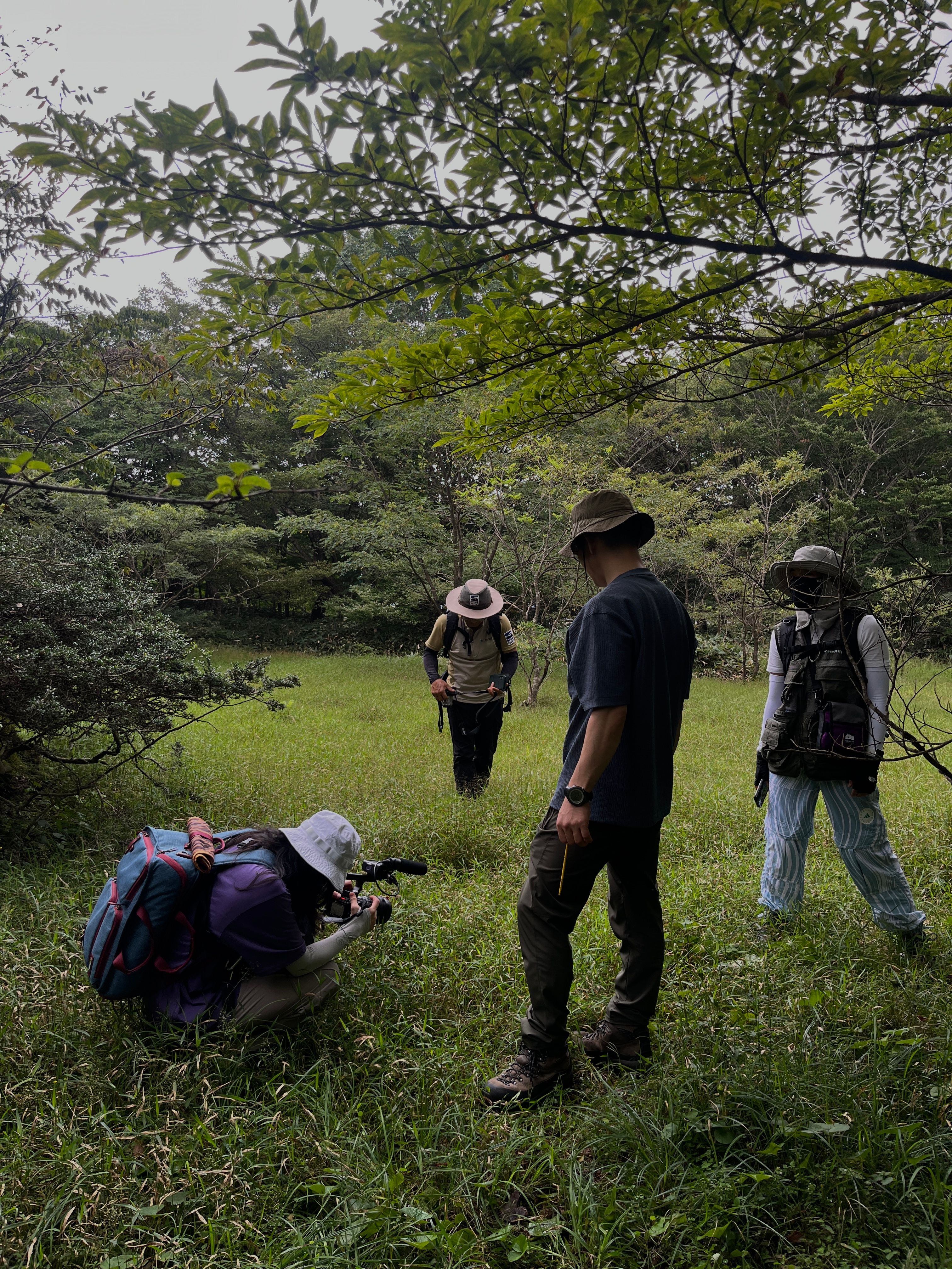 A group of people in a grassy clearing, with one person crouching to take a photo.