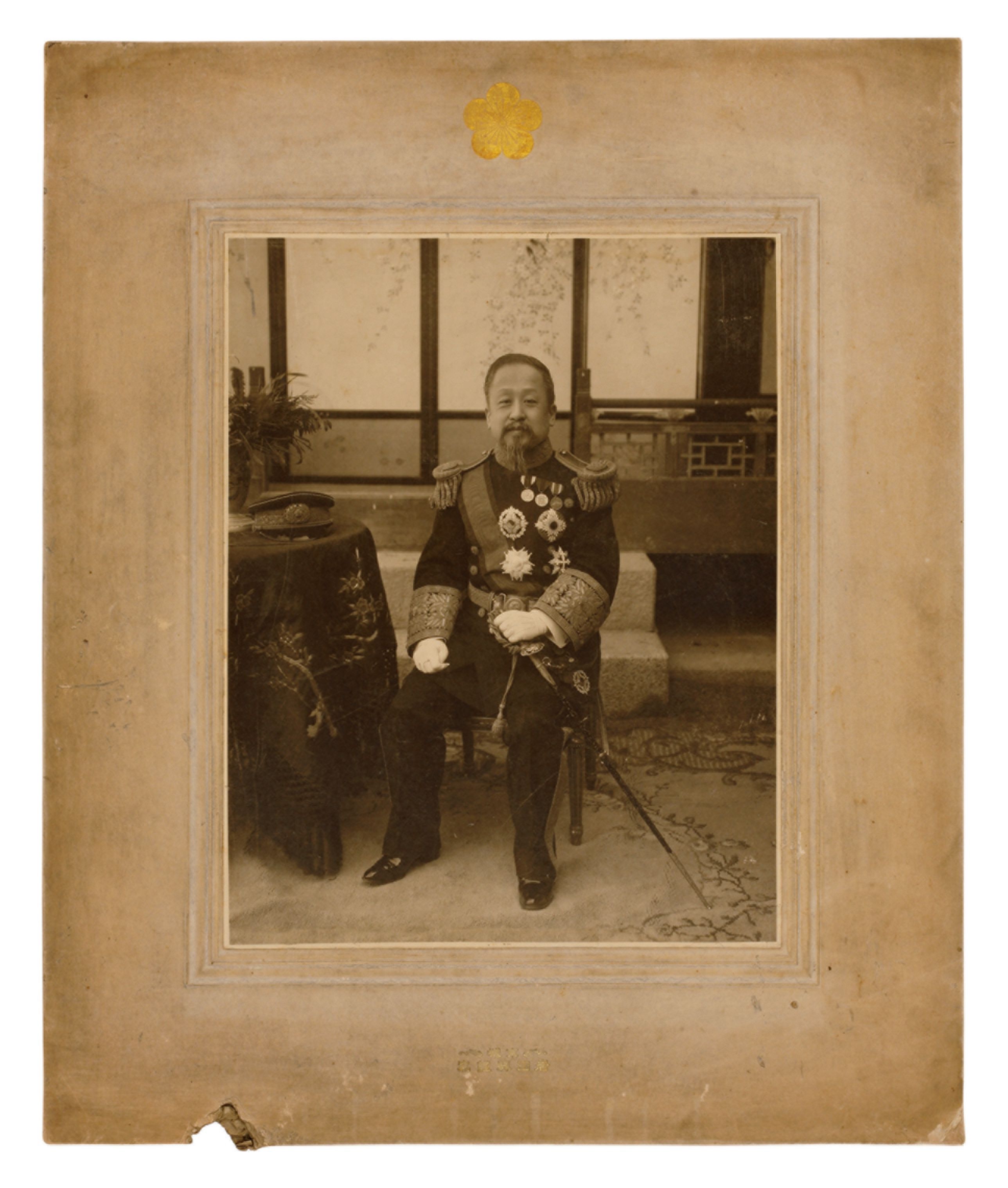 A vintage, sepia-toned photograph of Emperor Gojong from 1909. He is seated, clad in an ornate uniform, and captured in so...