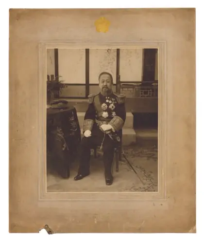 A vintage, sepia-toned photograph of Emperor Gojong from 1909. He is seated, clad in an ornate uniform, and captured in so...