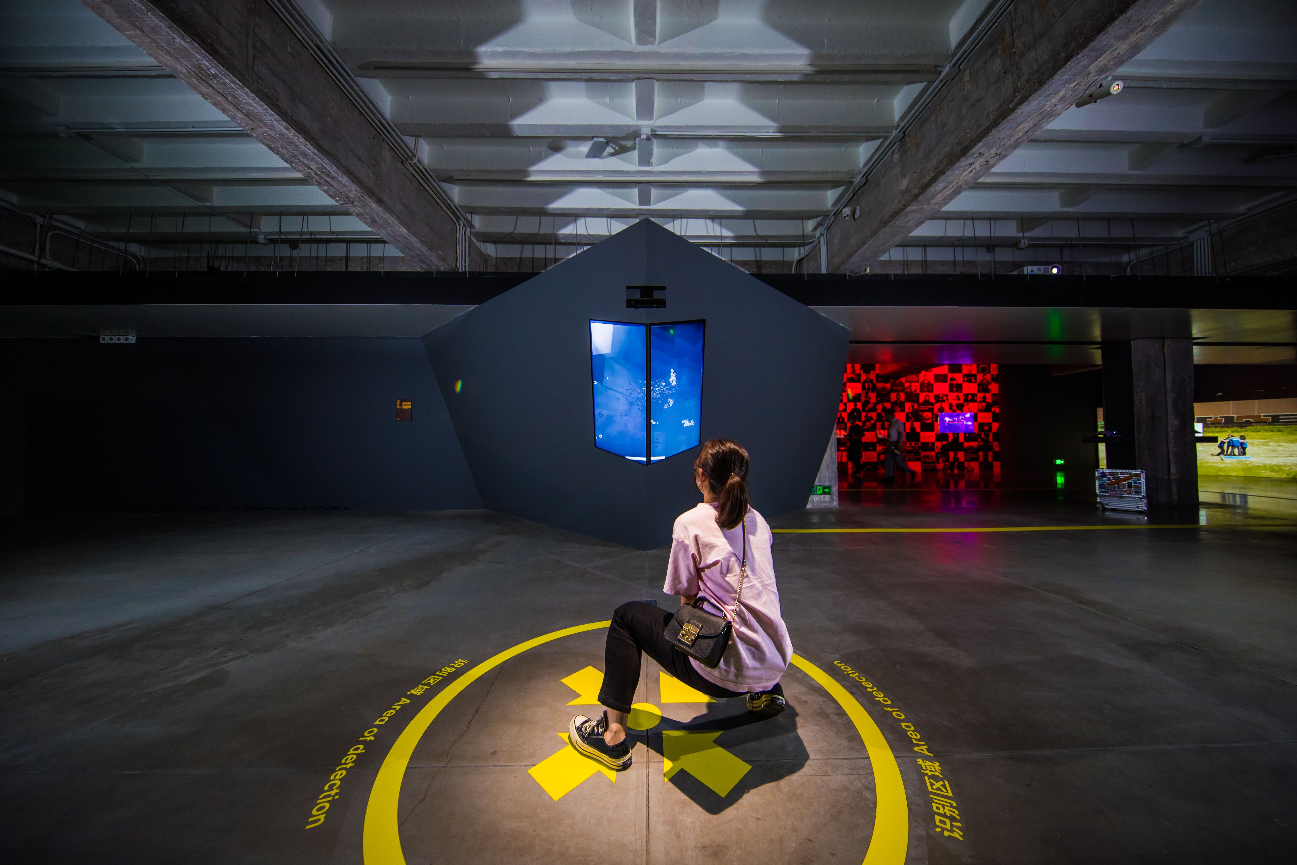 Person sitting on floor viewing abstract blue video installation in gallery.