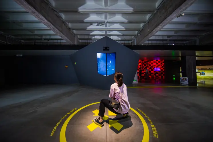Person sitting on floor viewing abstract blue video installation in gallery.