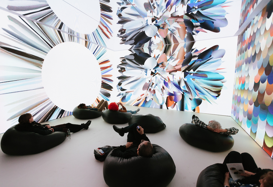 People lounging on bean bags, observing kaleidoscopic abstract images projected onto surrounding walls.