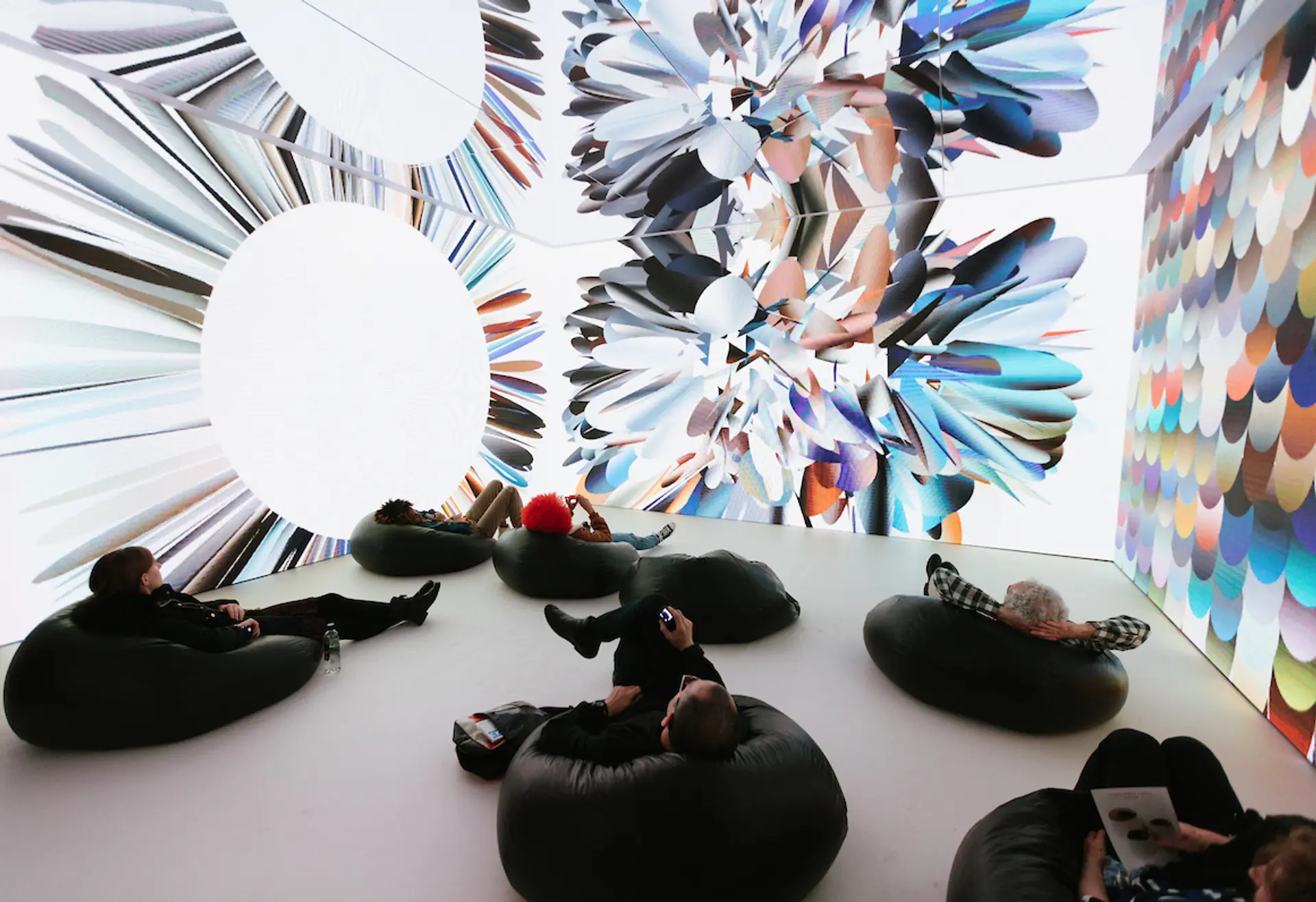 People lounging on bean bags, observing kaleidoscopic abstract images projected onto surrounding walls.