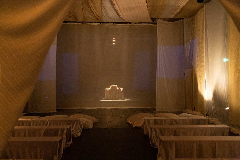 A minimalist performance space with draped white curtains and dim lighting, creating a serene ambiance.