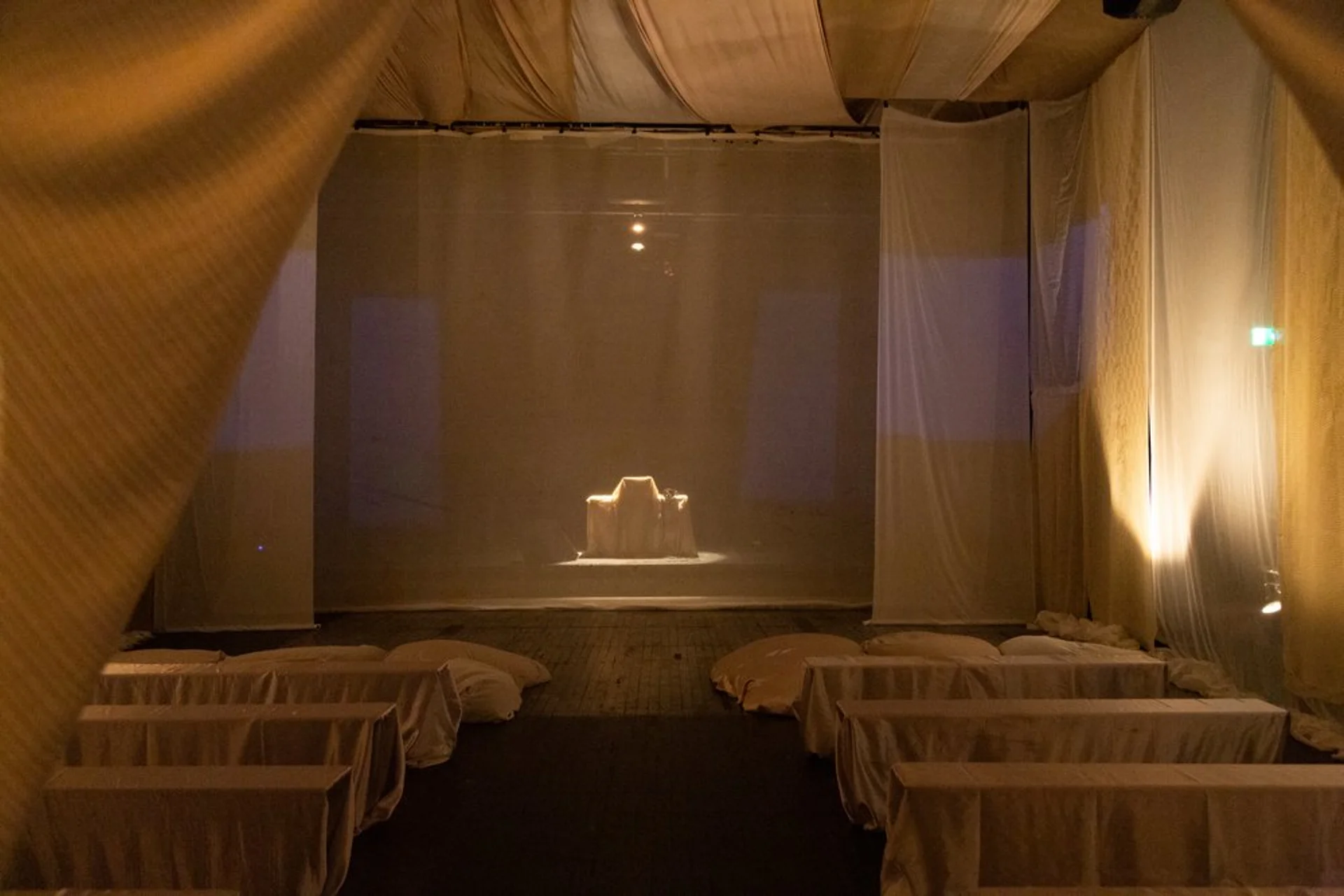 A minimalist performance space with draped white curtains and dim lighting, creating a serene ambiance.