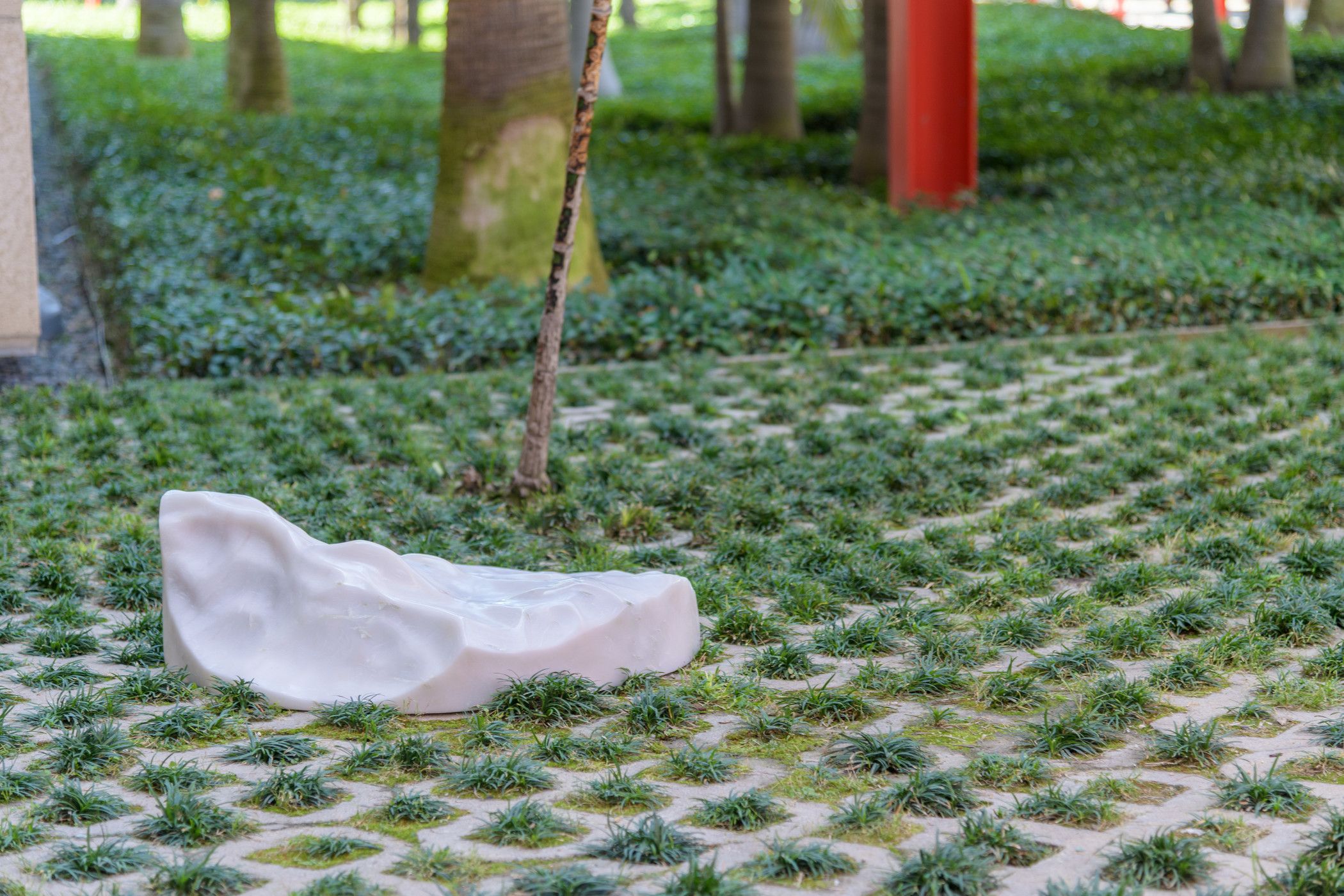 An abstract, white sculpture rests on a green, landscaped terrain. The form appears organic, resembling an oversized pebbl...