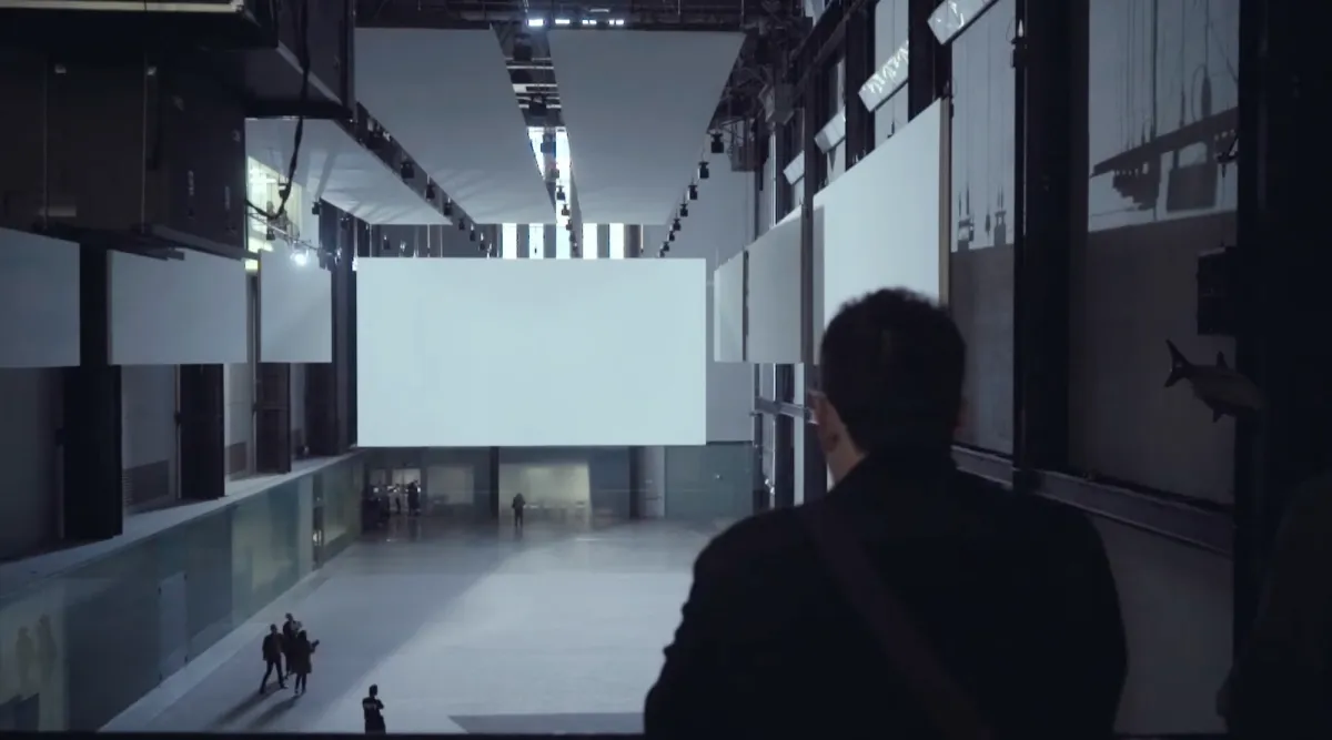 A person is standing, facing a vast gallery space. The room is adorned with large, clean white panels mounted on the walls.
