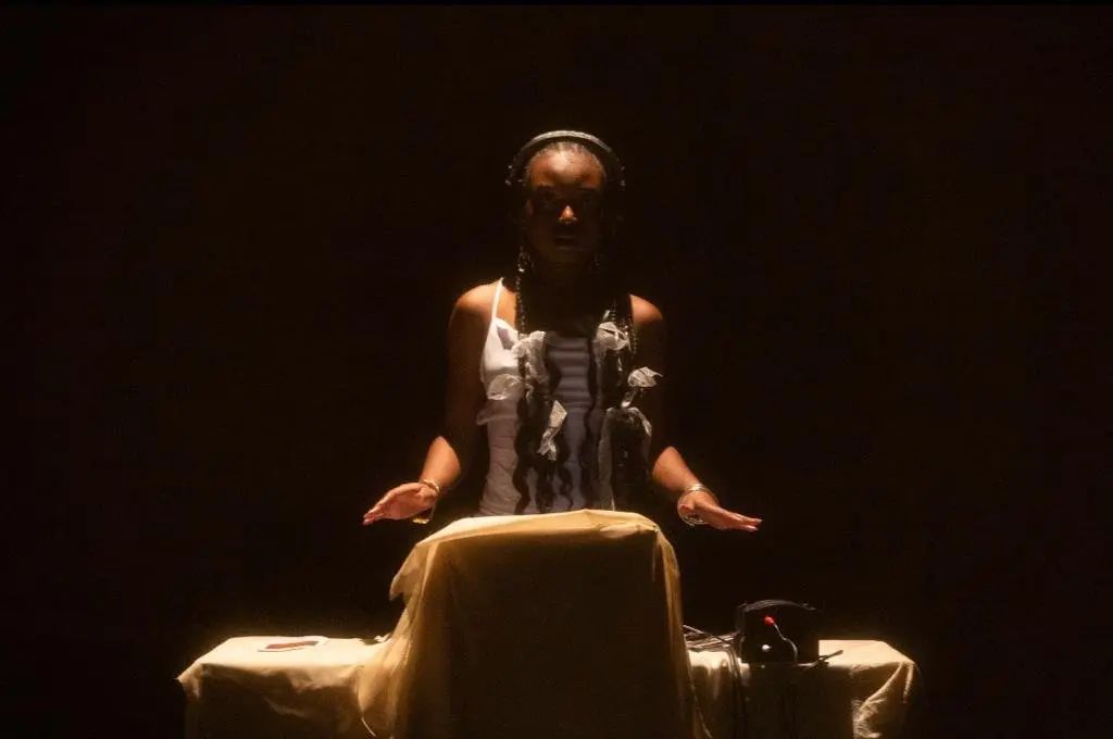 A woman performing a ritual or presentation, illuminated by a spotlight in a dark room.