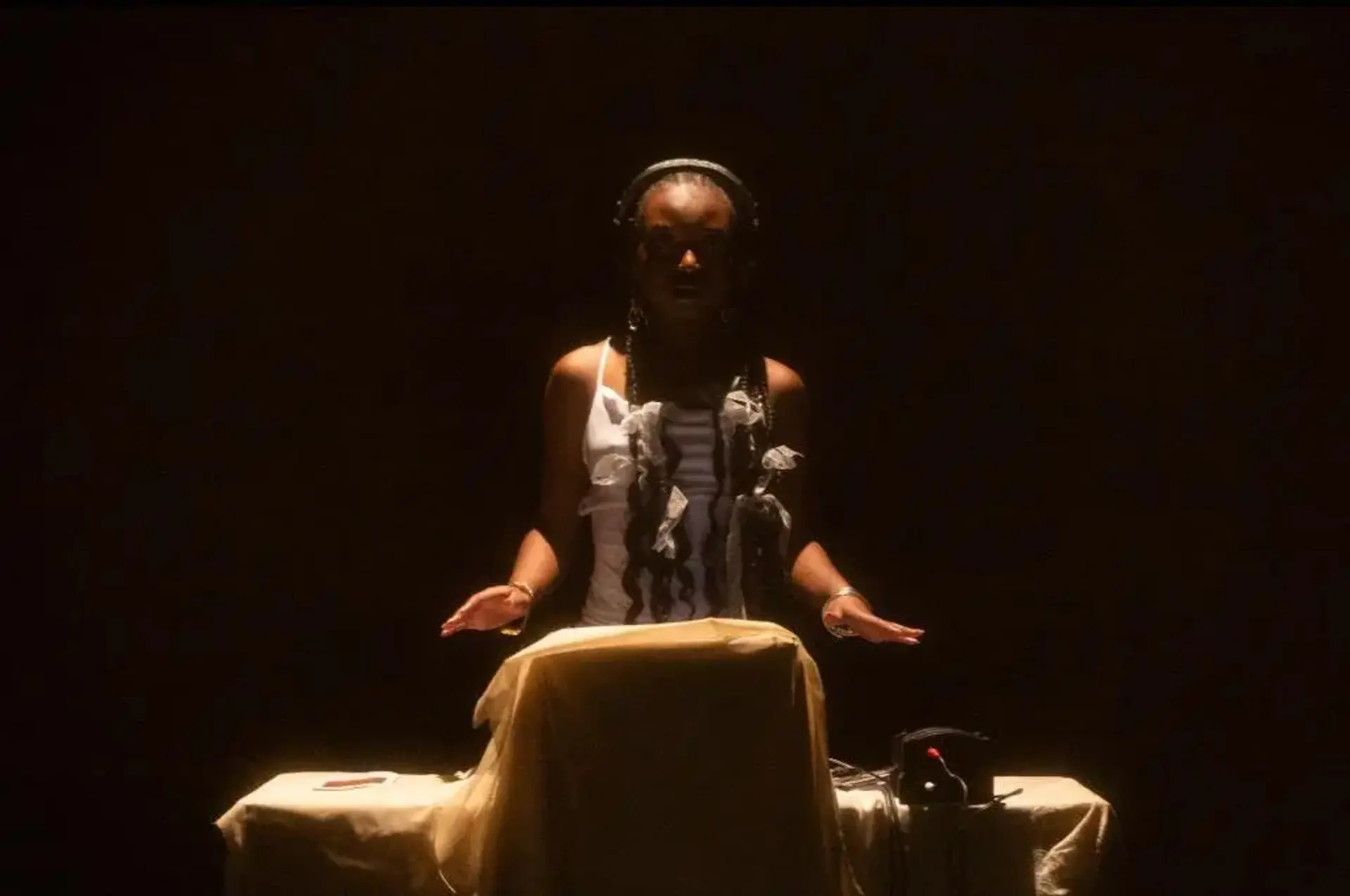 A woman performing a ritual or presentation, illuminated by a spotlight in a dark room.