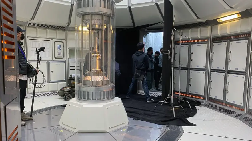 An indoor environment, reminiscent of a spaceship interior, featuring a central glass cylinder with individuals engaged in...