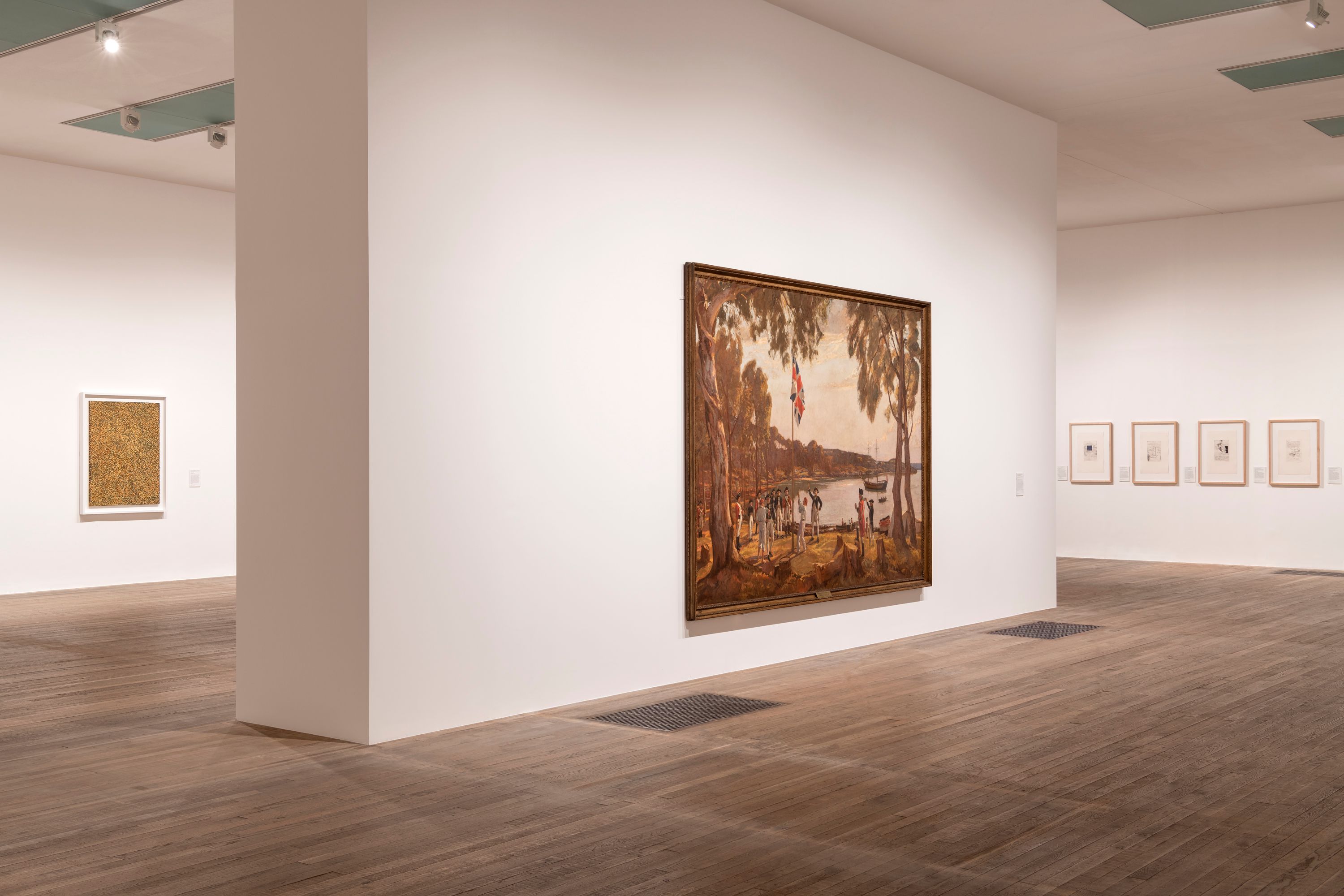 An art gallery showcasing numerous pieces of artwork displayed on stark white walls, contrasted by a polished wooden floor...