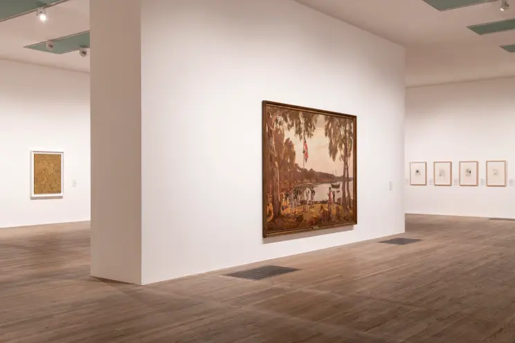 An art gallery showcasing numerous pieces of artwork displayed on stark white walls, contrasted by a polished wooden floor...