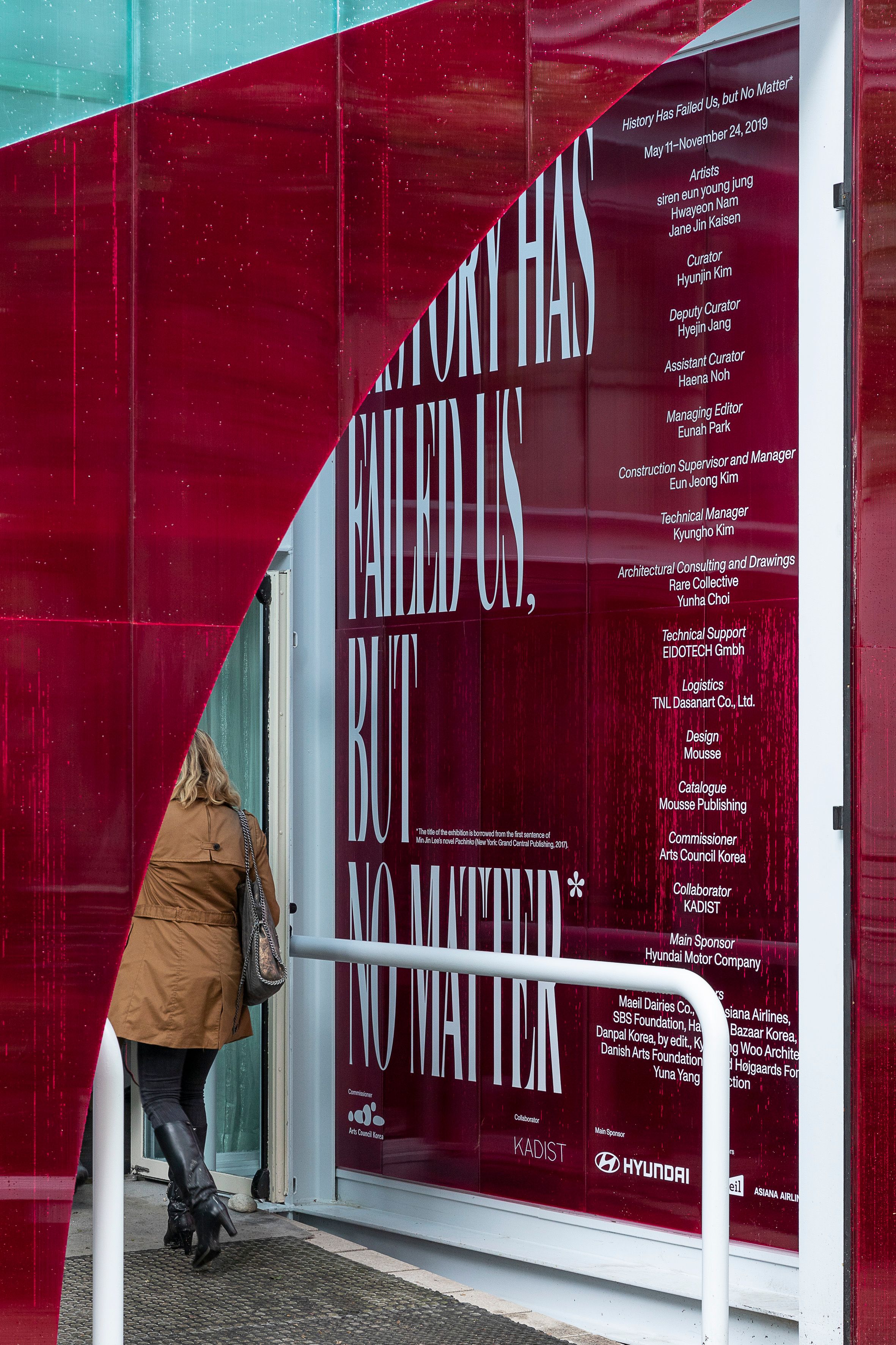 A vibrant red information wall, part of the Korean Pavilion at the Venice Biennale 2019, featuring exhibition details.