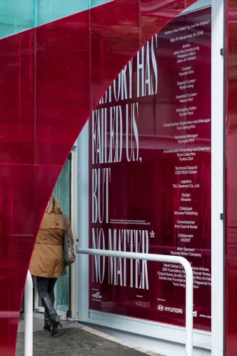 A vibrant red information wall, part of the Korean Pavilion at the Venice Biennale 2019, featuring exhibition details.