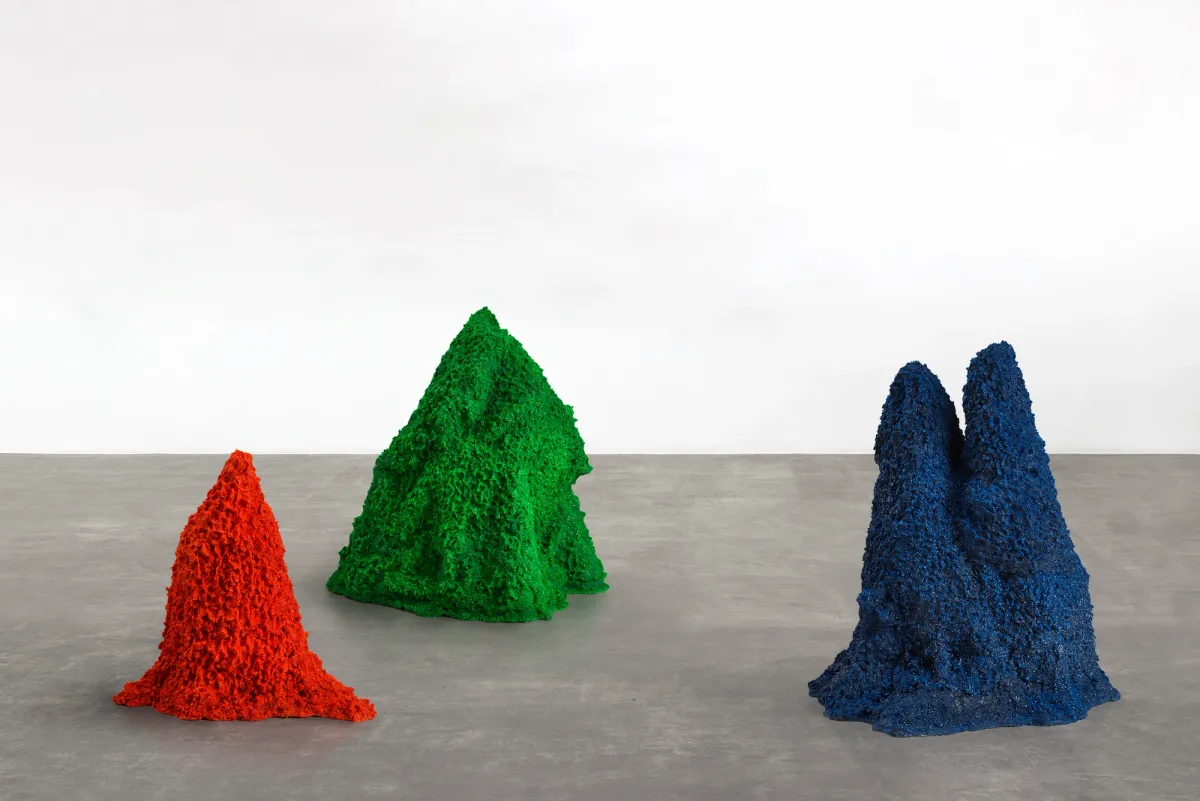 Three mounds crafted from colored sand, each a different color: red, green, and blue.
