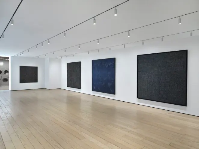 Minimal gallery with large dark abstract canvases on white walls, evenly lit, with spacious wooden floor.