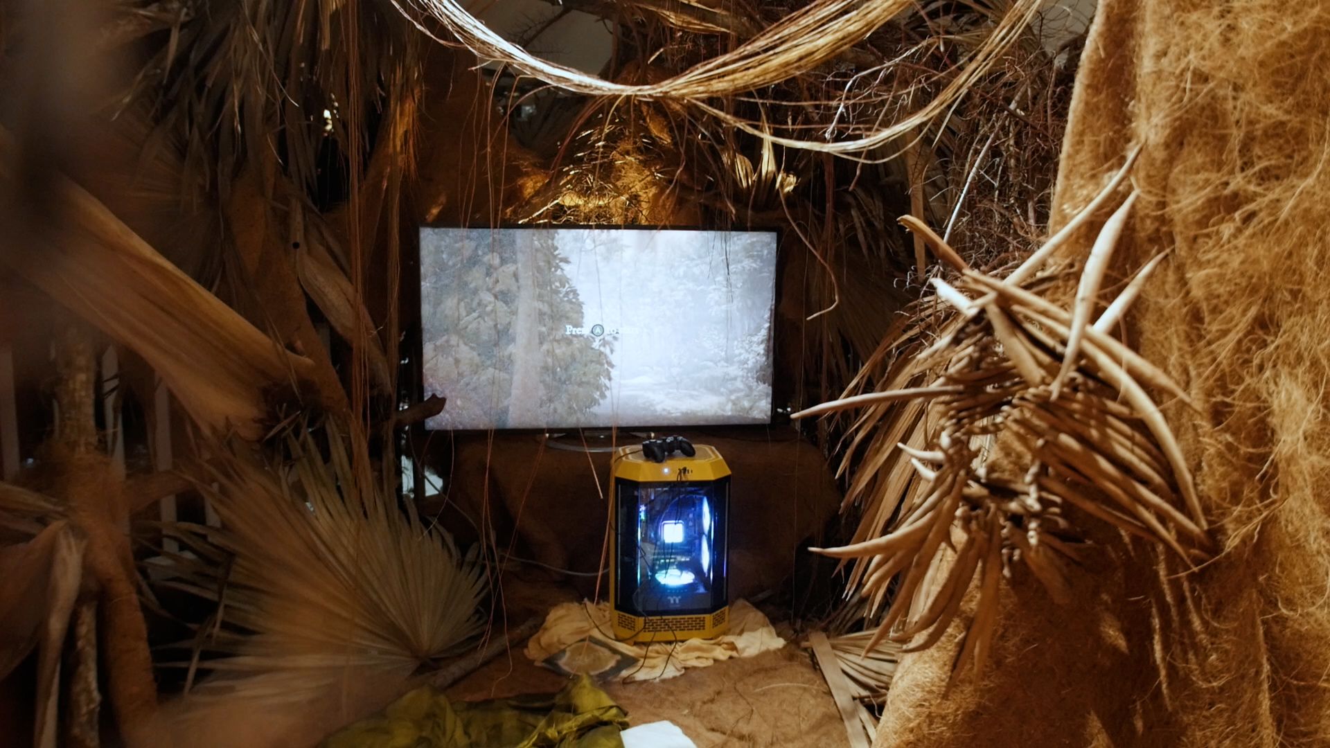 Close-up of a nature-inspired installation with a gaming monitor and console encased in yellow lighting.