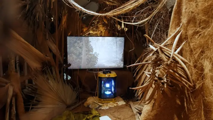 Close-up of a nature-inspired installation with a gaming monitor and console encased in yellow lighting.
