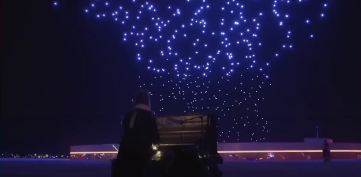 A person seated at a piano in a dimly lit room, surrounded by a constellation of glowing blue dots.